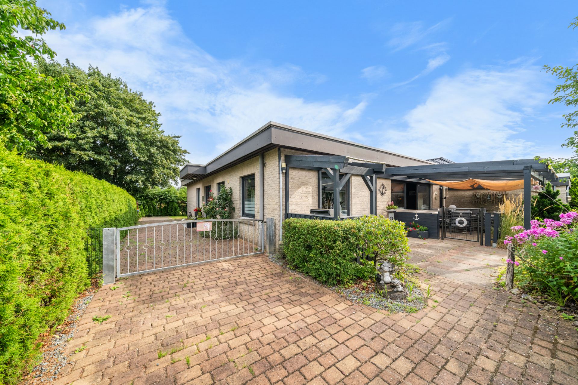 Einfamilienhaus mit gepflasterter Einfahrt, Gartenhecken und überdachter Terrasse.