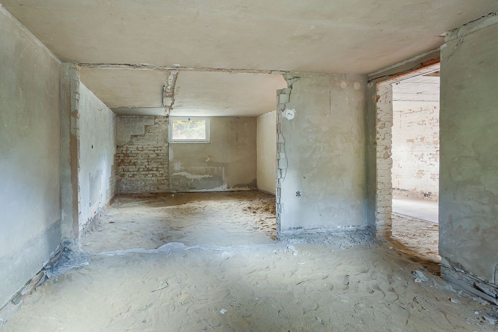 Leerer Raum mit unverputzten Wänden, offenem Durchgang und kleinem Fenster.