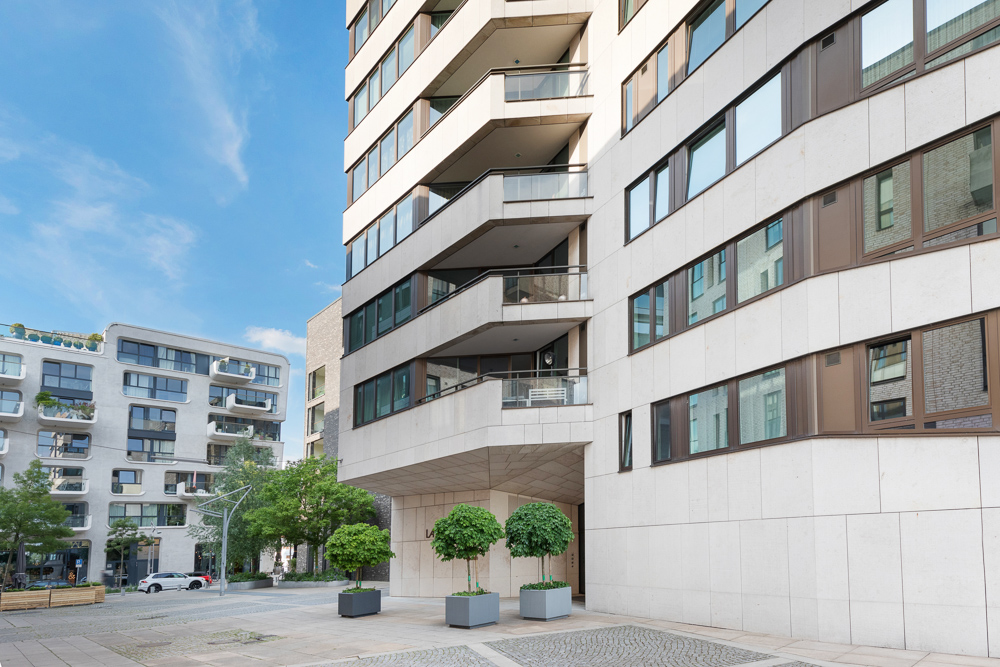 Moderne Wohngebäude mit Balkonen und großen Fenstern, davor stehen zwei Bäume in Pflanzkübeln.