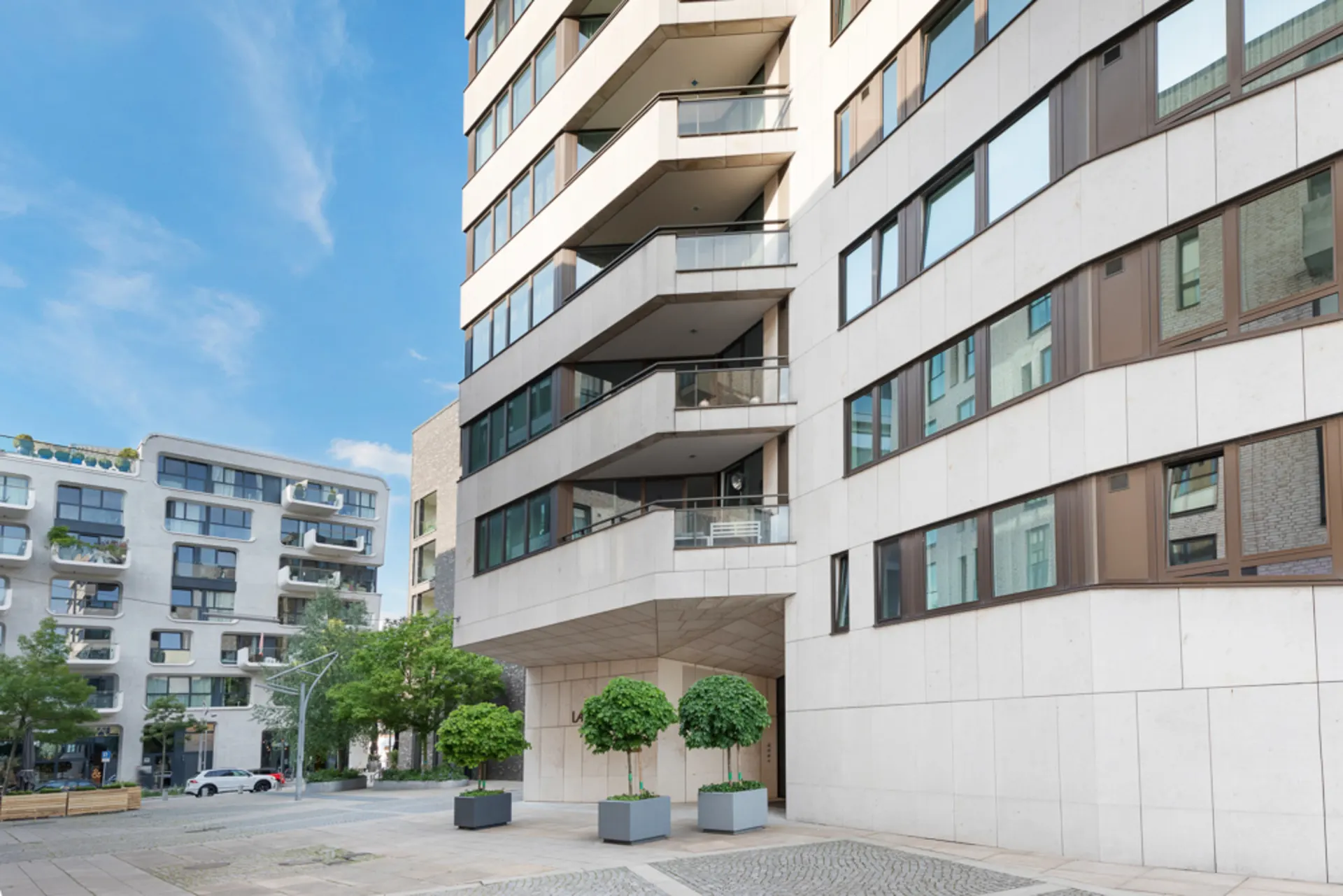 Moderne Wohngebäude mit Balkonen und großen Fenstern, davor stehen zwei Bäume in Pflanzkübeln.