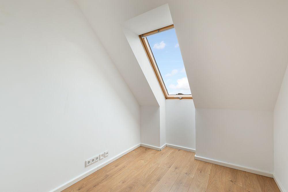 Helles Zimmer mit Dachschräge, Holzfußboden und großem Dachfenster.