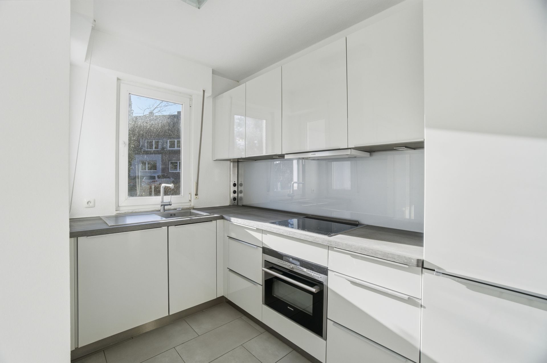 Helle moderne Einbauküche mit weißen Schränken, Fenster, Herd, Spüle und Einbauofen.