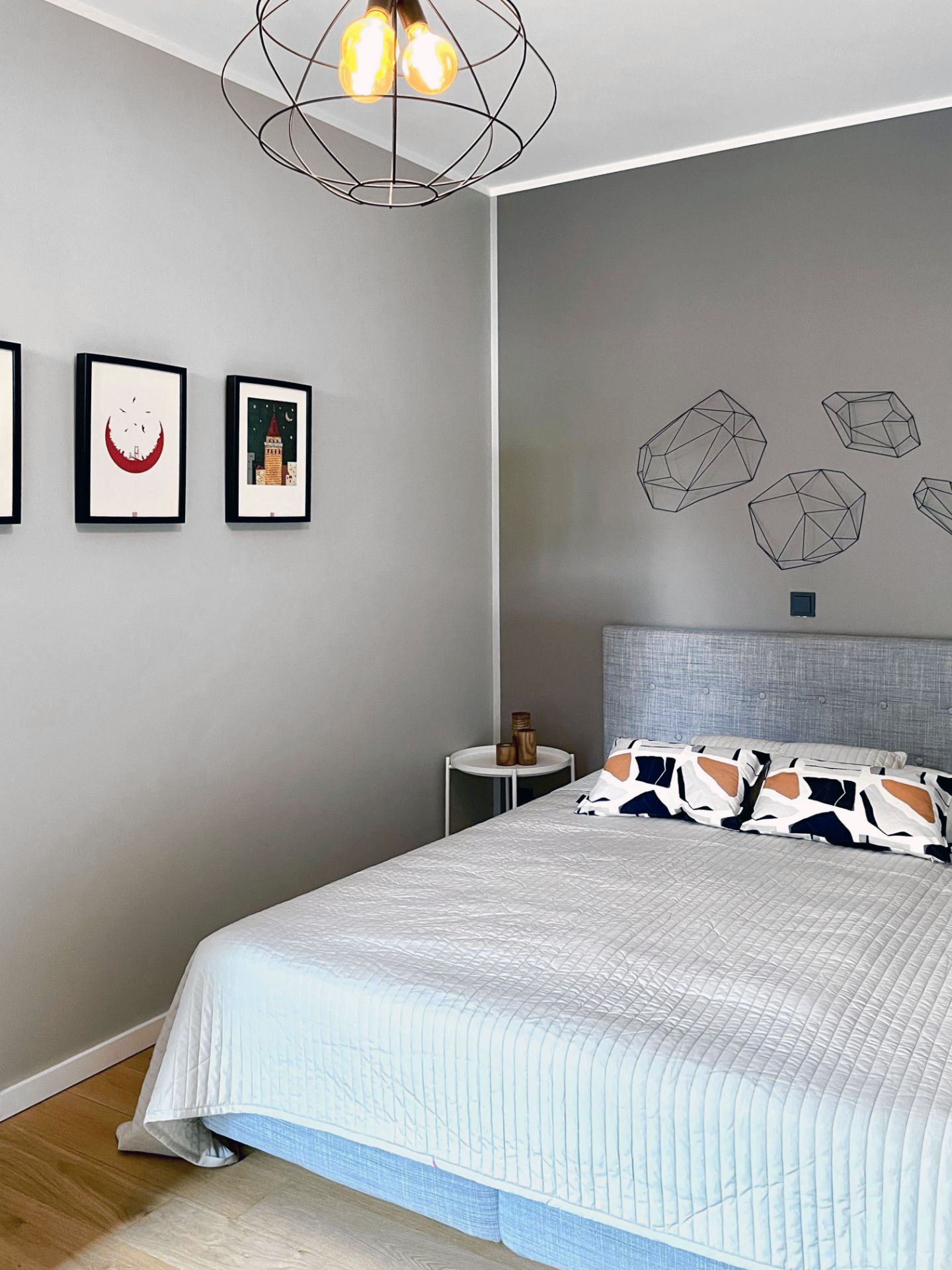 Modernes Schlafzimmer mit grauer Wand, Doppelbett, Nachttisch und Wandbildern.