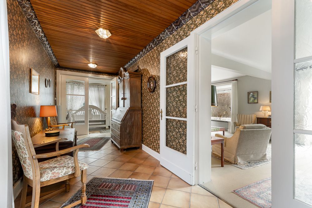 Flur mit Holzboden und gemusterter Tapete, Blick ins helle Wohnzimmer und Schlafzimmer.