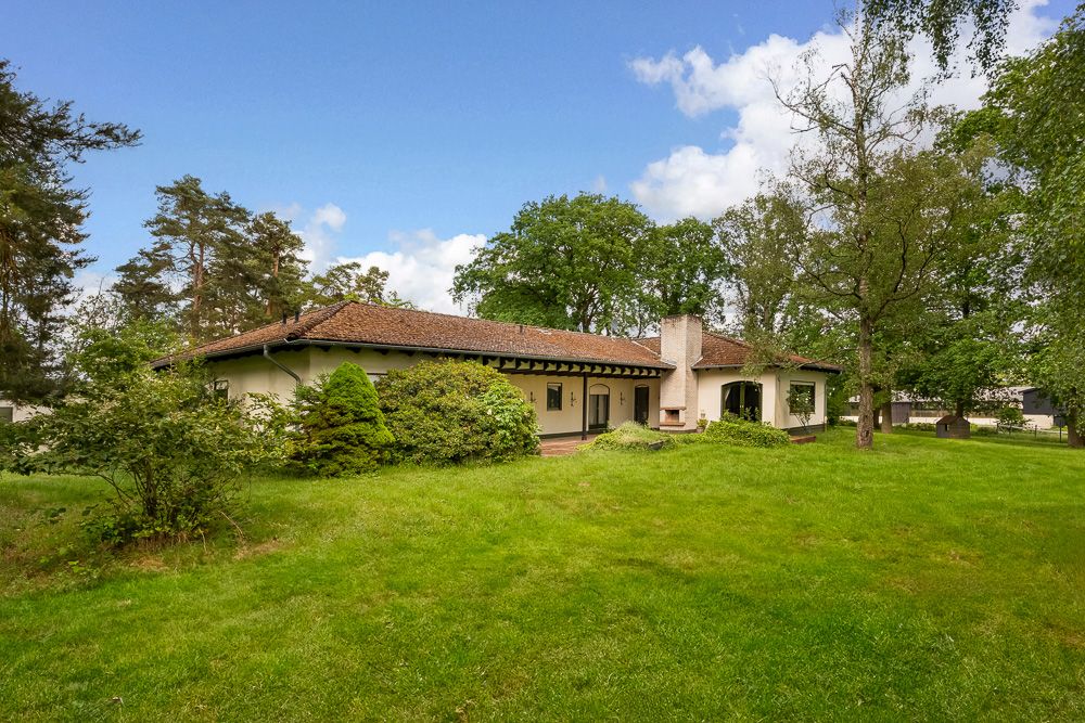 Einfamilienhaus mit Flachdach und großem Garten, umgeben von Bäumen und viel Grün.