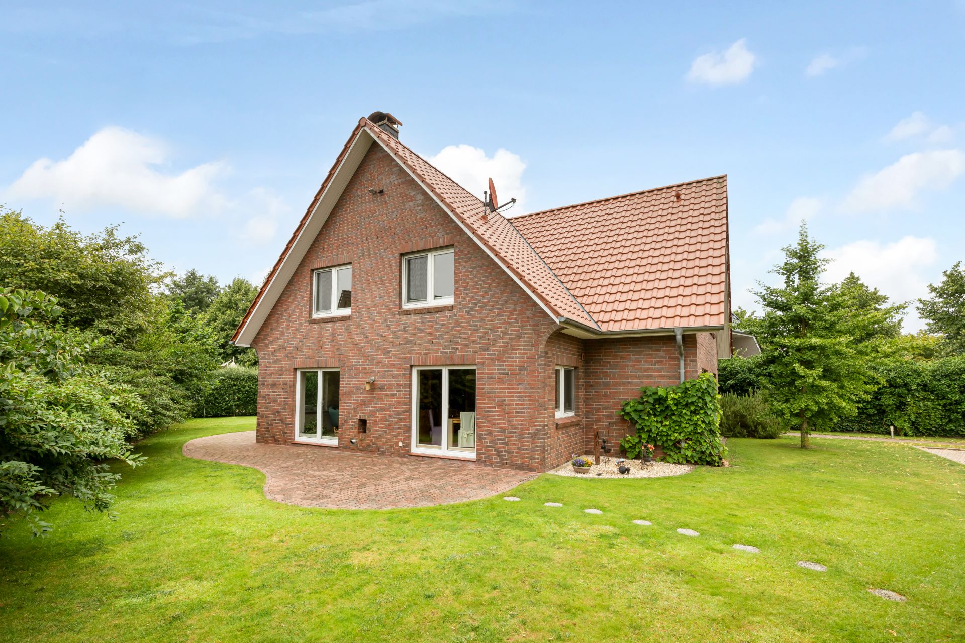 Backsteinwohnhaus mit Satteldach und Garten, große Fenster und Terrasse im Grünen.