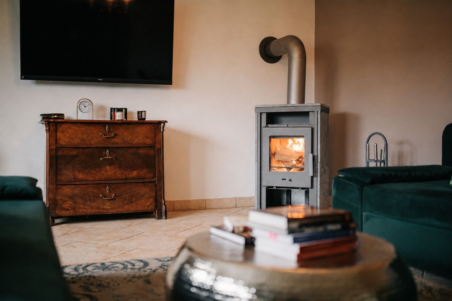 Wohnzimmer mit Holzofen, grünem Sofa, Holztisch, Kommode und Wandfernseher.