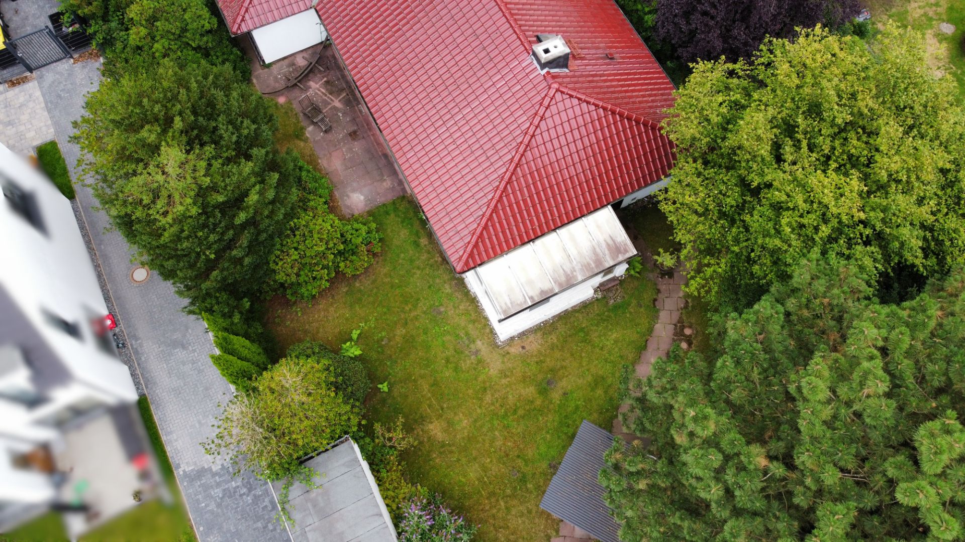 Luftaufnahme eines Hauses mit rotem Dach und großem Garten mit vielen Bäumen.