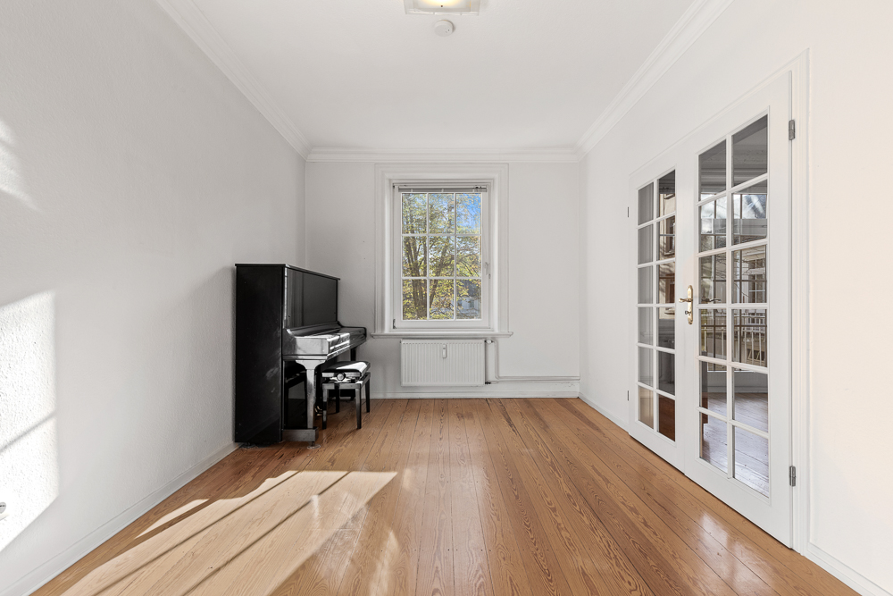 Helles Zimmer mit Holzboden, Fenster, Glastüren und schwarzem Klavier.