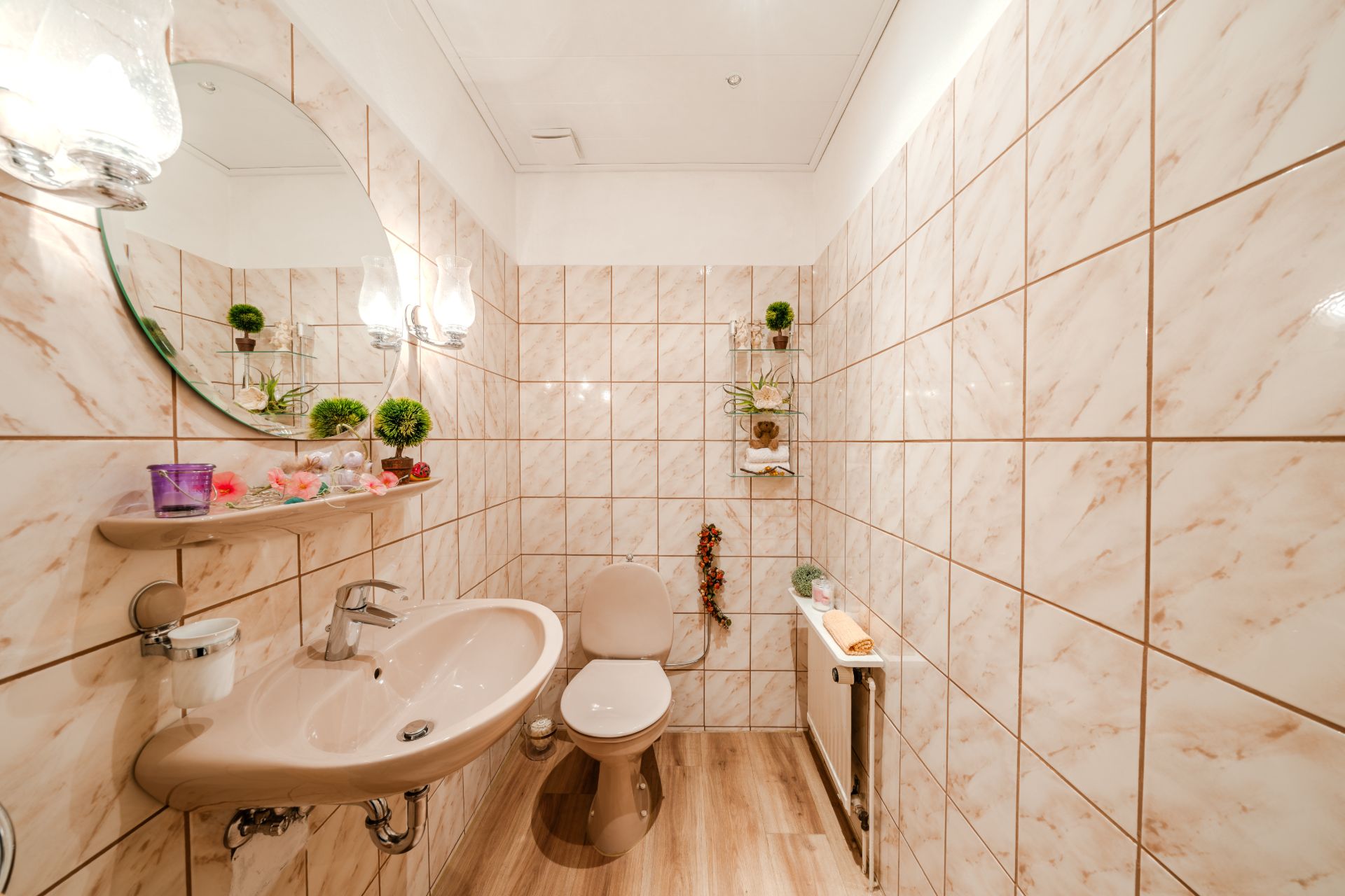 Kleines Bad mit beigem Waschbecken, Toilette, Spiegel und dekorativen Pflanzen auf Regalen.