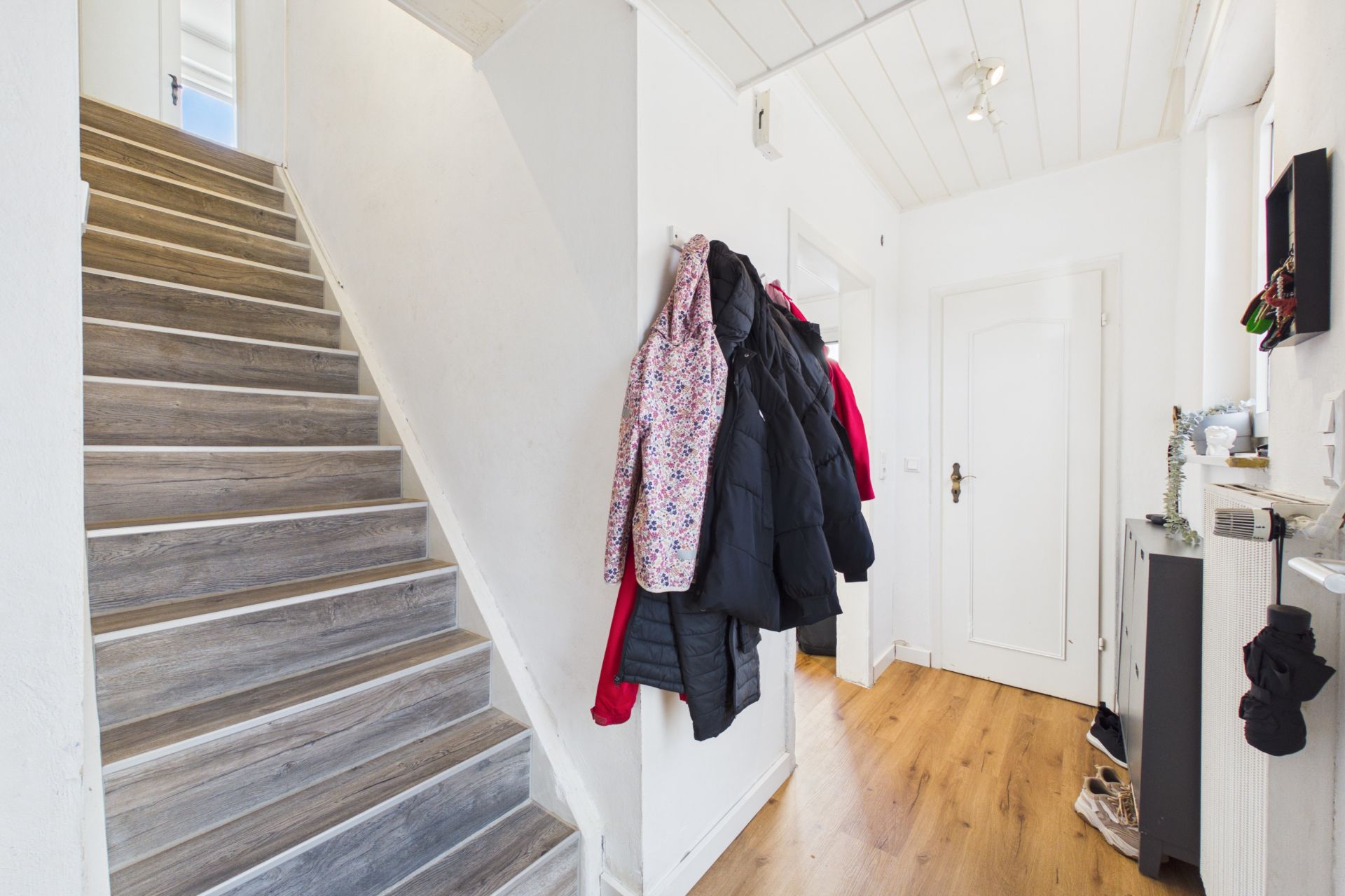 Flur mit Treppe, Holzboden, Garderobe und Jacken an Haken.