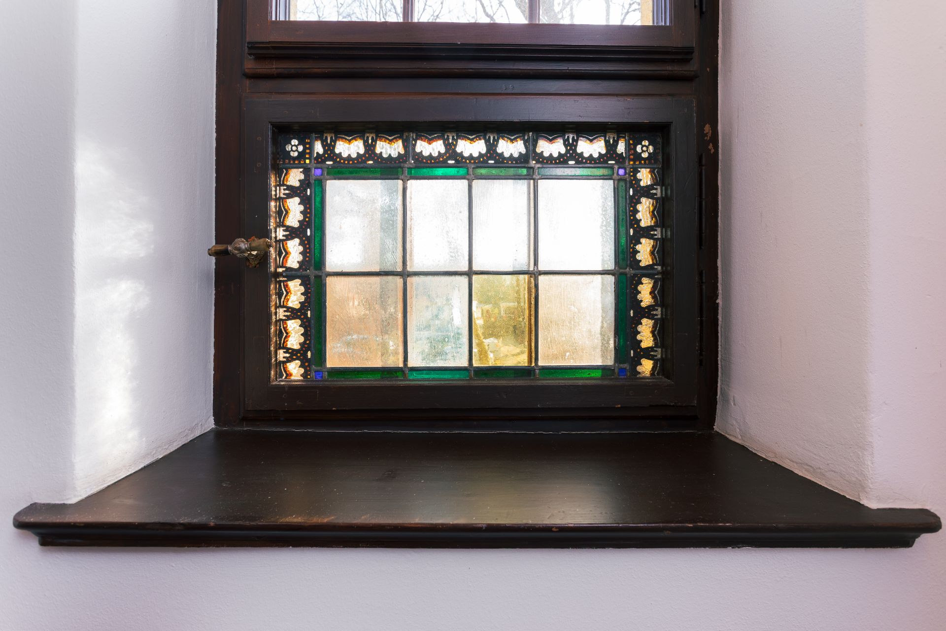 Kleines Fenster mit buntem Glas und dunklem Holzrahmen auf einer Fensterbank.