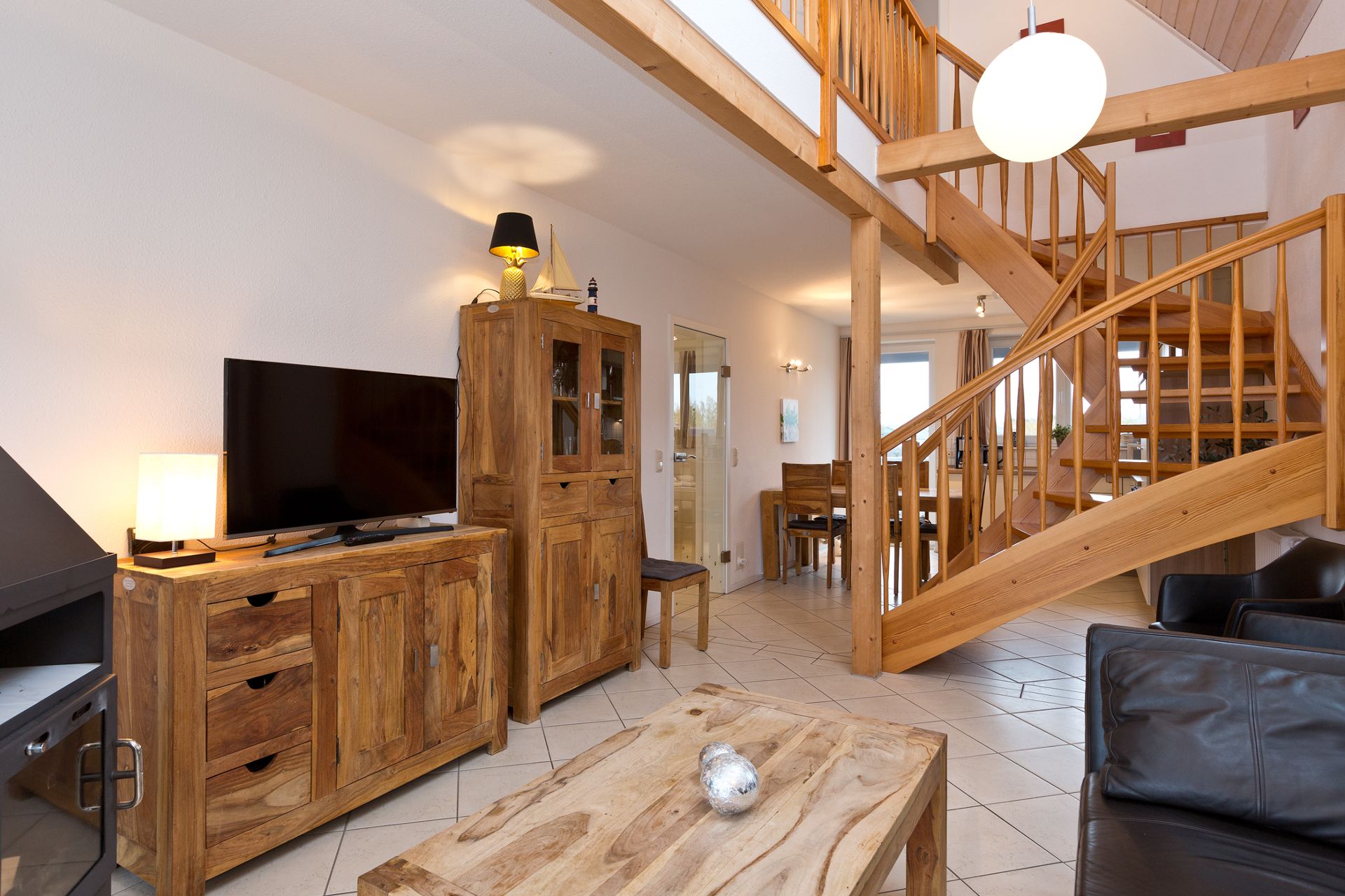 Wohnzimmer mit Holzmöbeln, Fernseher, Ledersessel und offener Holztreppe.