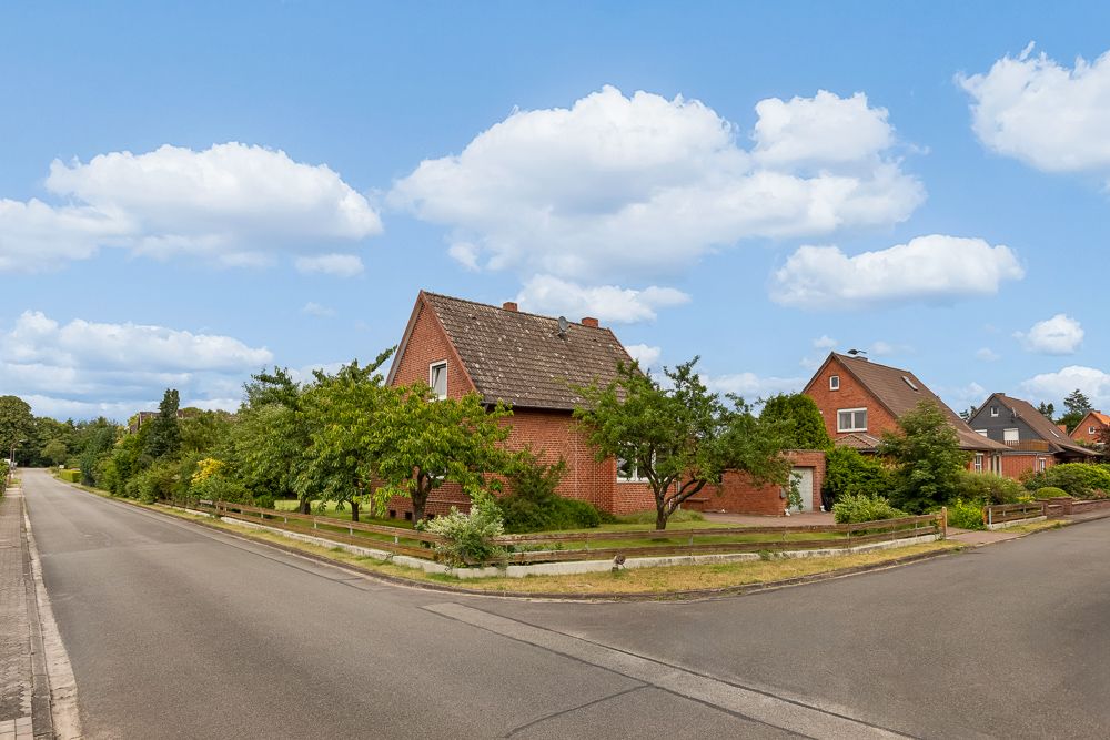 Backsteinhaus mit Garten an einer ruhigen Straßenecke, umgeben von Bäumen und weiteren Wohnhäusern.
