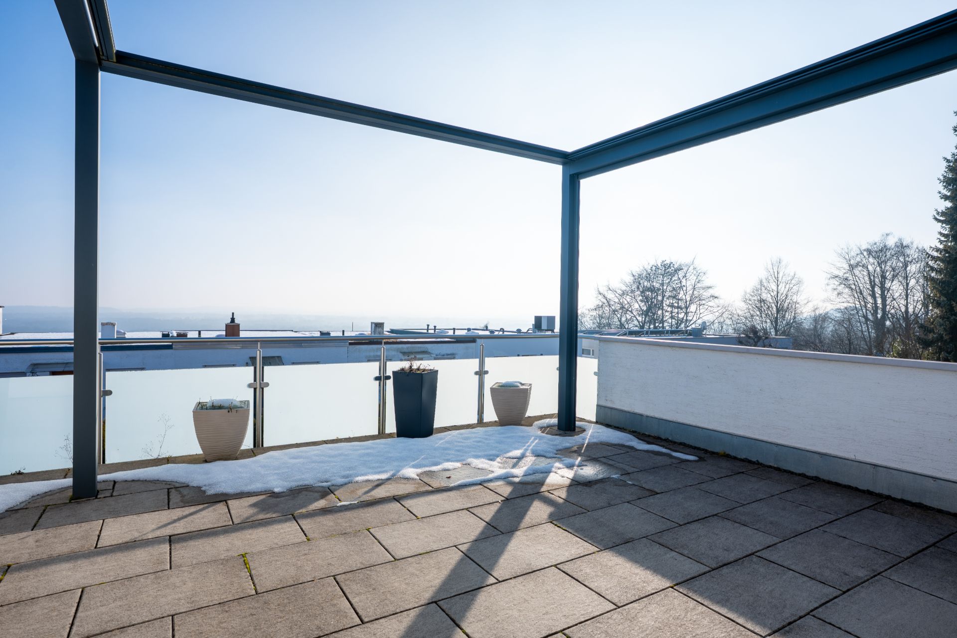 Große Terrasse mit Fliesenboden, Überdachungsrahmen und Blumenkübeln, teilweise mit Schnee bedeckt.