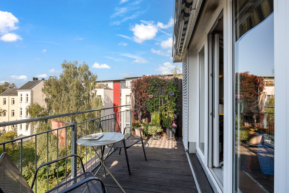 Balkon mit Tisch, Stuhl, Pflanzen und Blick auf Nachbarhäuser bei sonnigem Wetter.