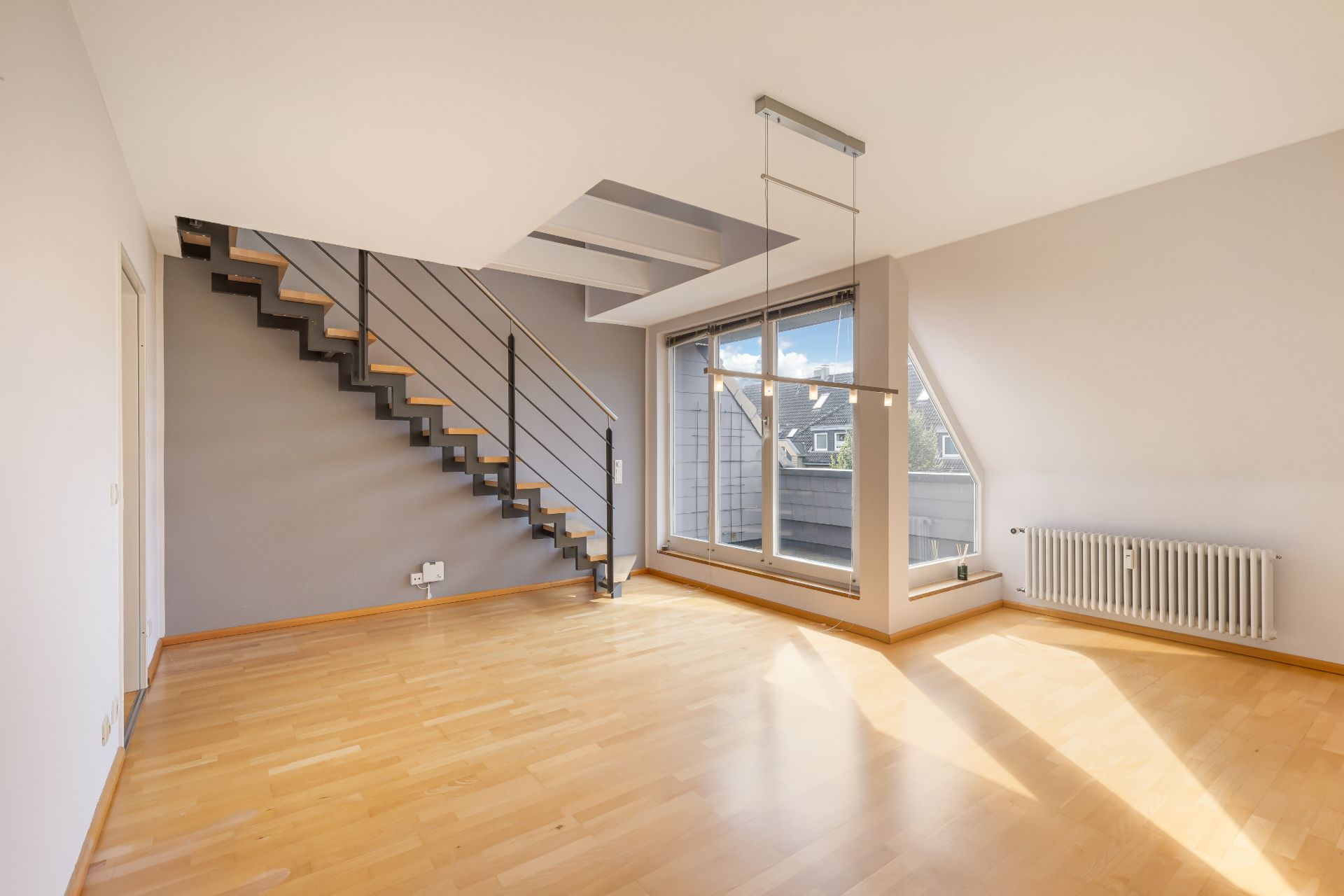 Helles Zimmer mit Holzfußboden, Treppe und großen Fenstern.