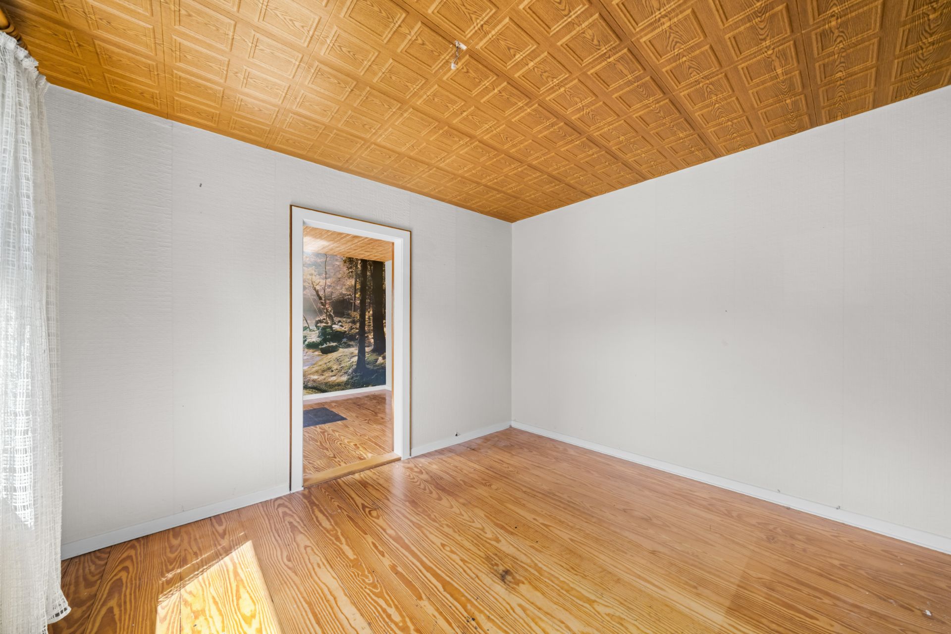 Leeres Zimmer mit Holzfußboden, heller Decke und Tür mit Blick nach draußen.