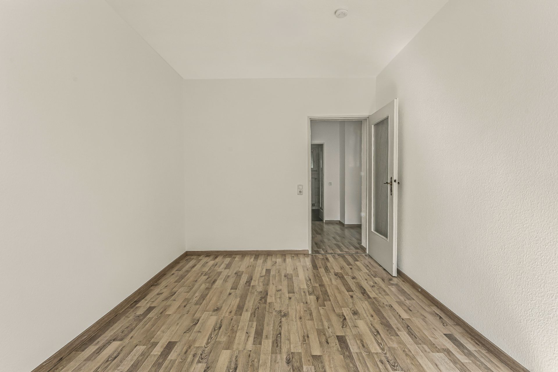 Leerer Raum mit Holzfußboden, weißen Wänden und offener Tür.