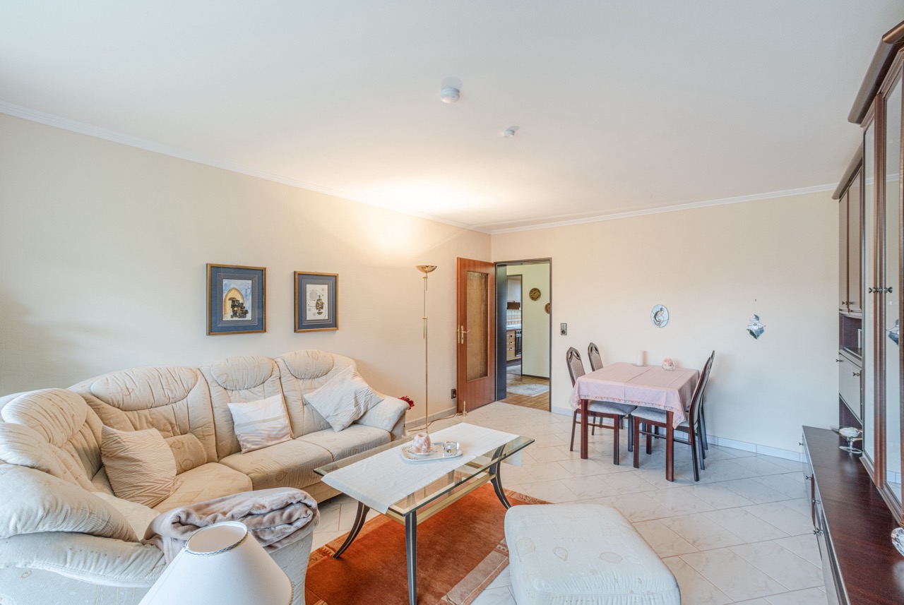 Helles Wohnzimmer mit cremefarbenem Sofa, Couchtisch, Essbereich und offener Tür zur Küche.