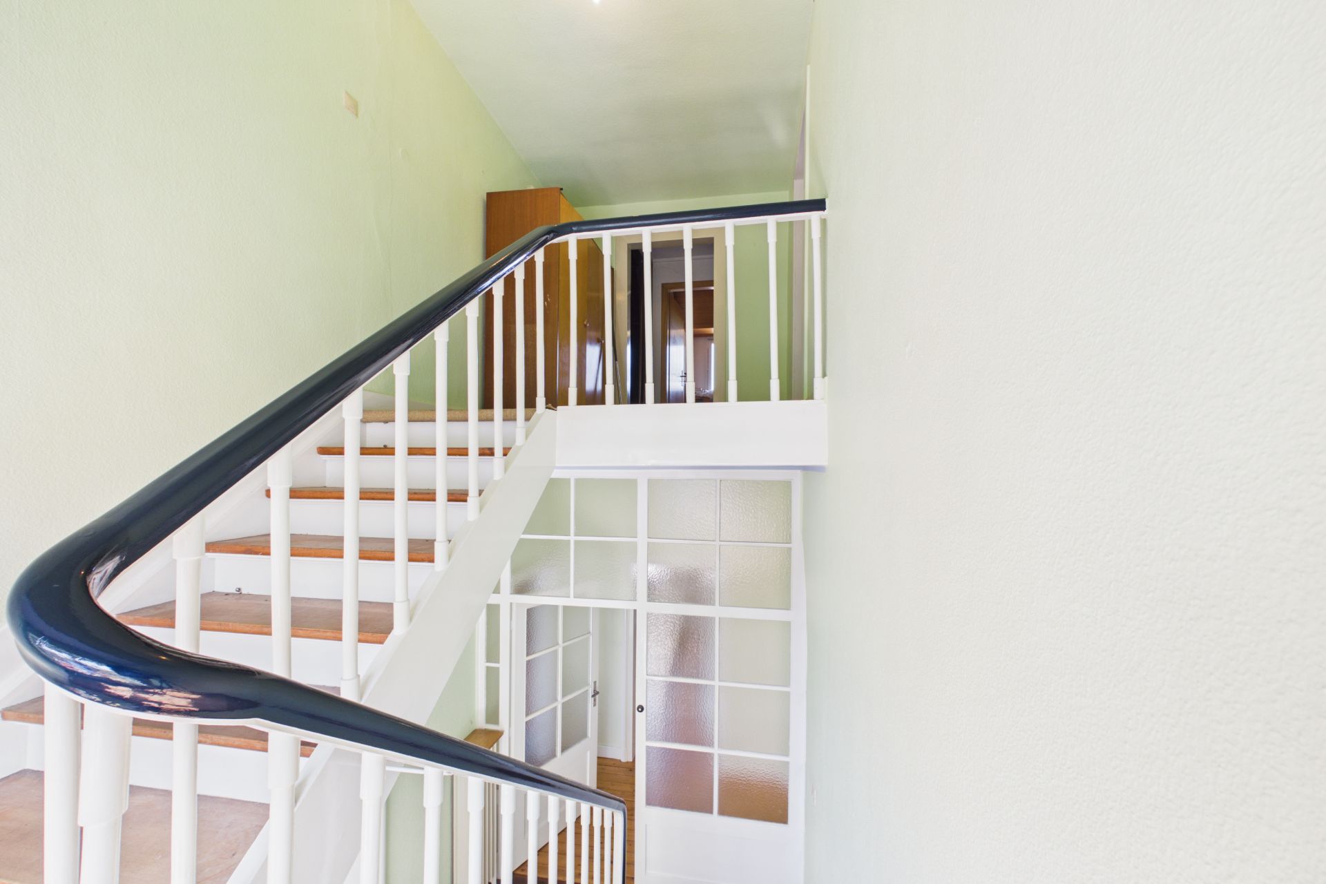 Weiße Treppe mit dunklem Handlauf und Glasflügeltür in einem Flur.