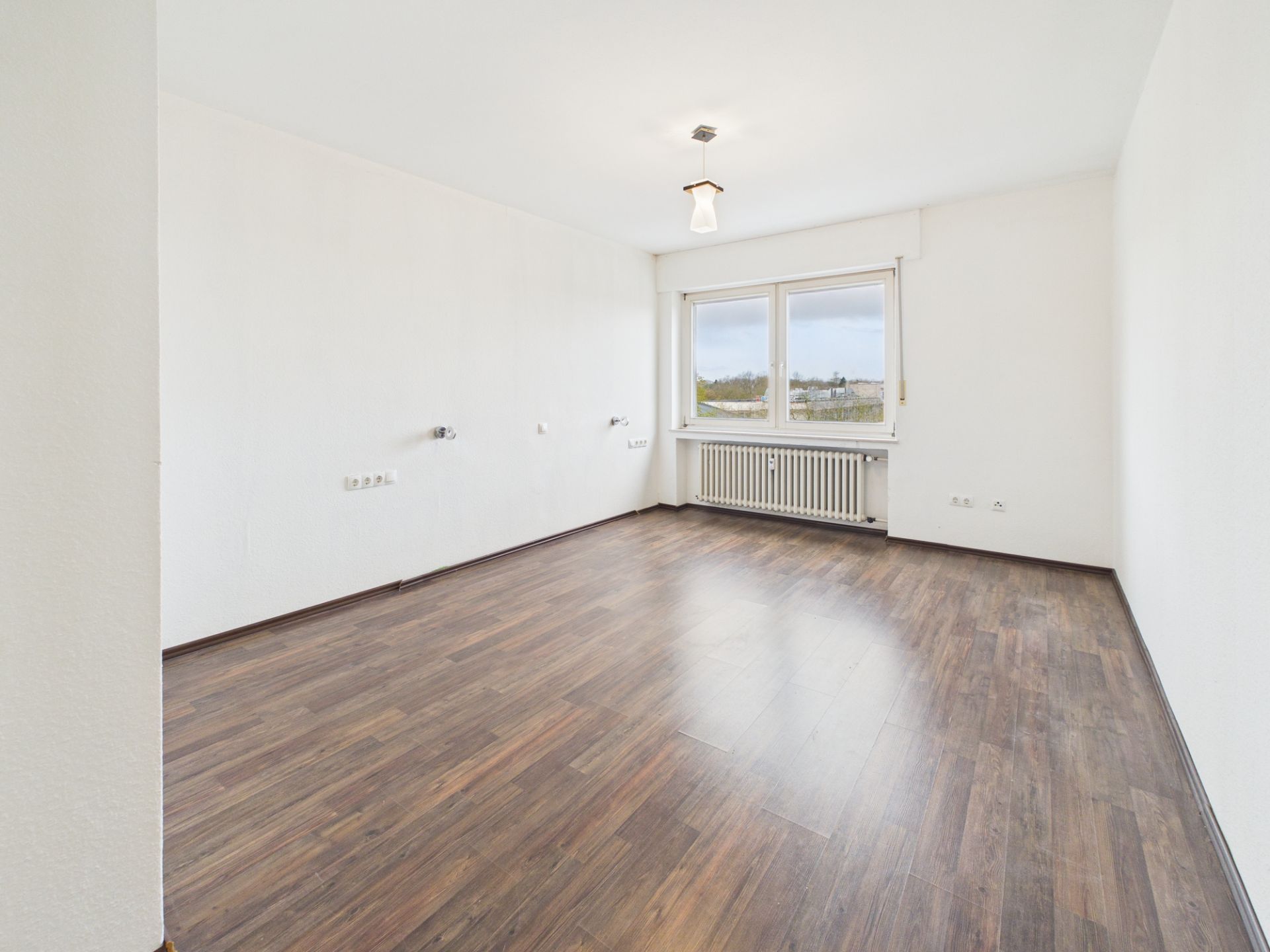 Leerer Raum mit dunklem Holzfußboden und großem Fenster.