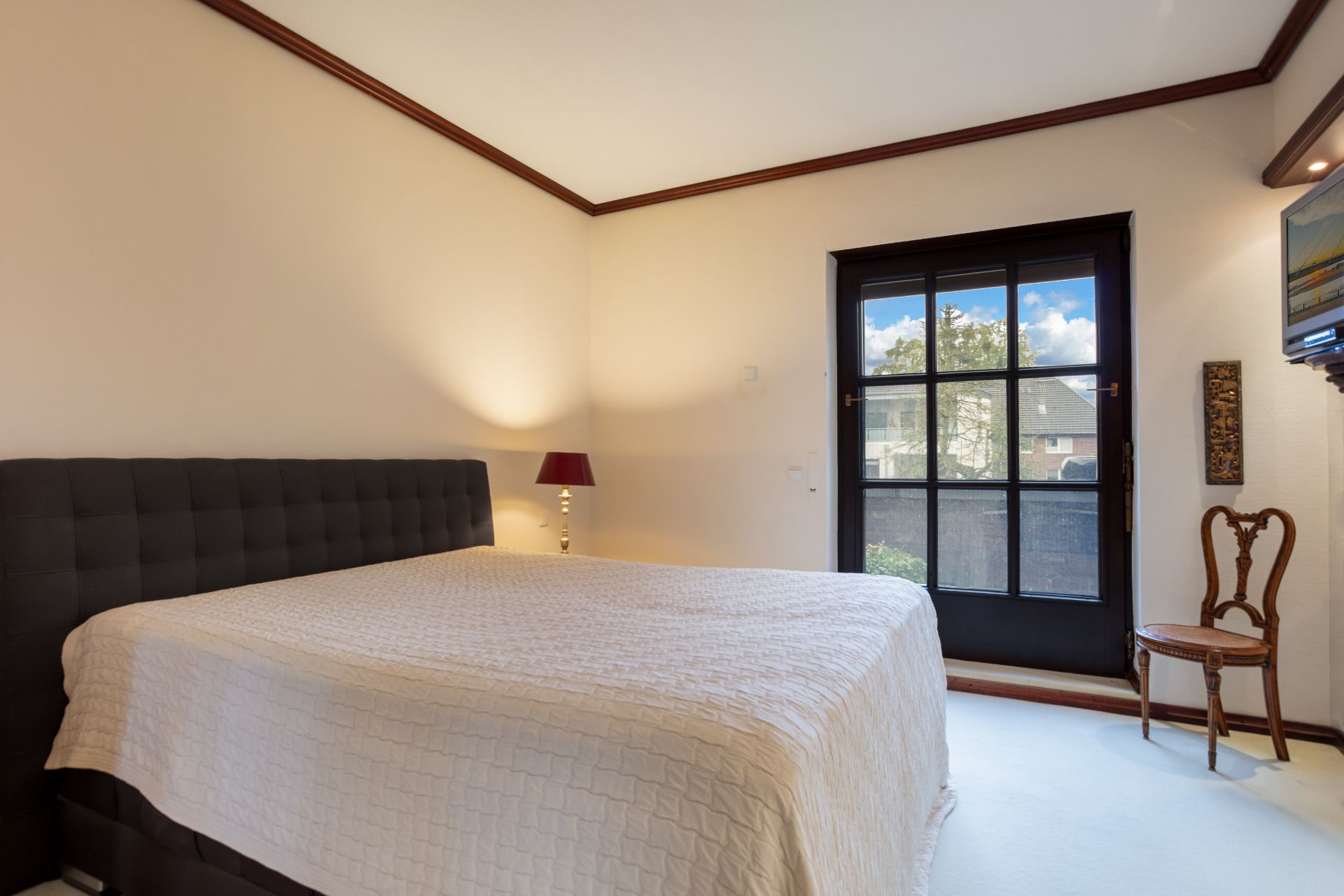 Schlafzimmer mit großem Bett, Nachttischlampe, Stuhl und Fenster mit Blick nach draußen.