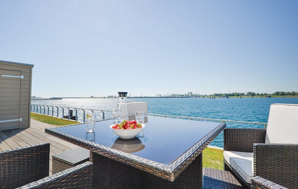 Terrasse mit Glastisch, Stühlen und Blick auf einen großen See bei sonnigem Wetter.
