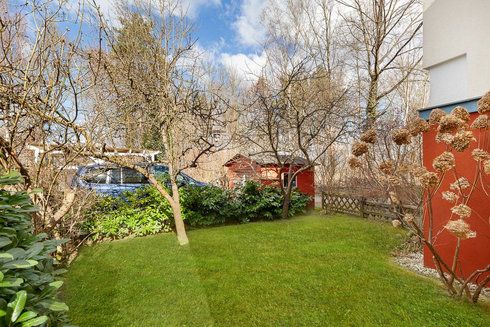 Garten mit grünem Rasen, Sträuchern, Bäumen, einem roten Schuppen und einem blauen Auto.