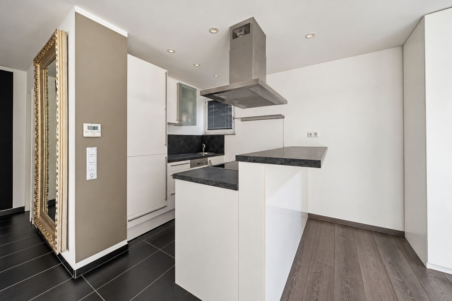 Moderne weiße Küche mit schwarzer Arbeitsplatte und großem Spiegel an der Wand.