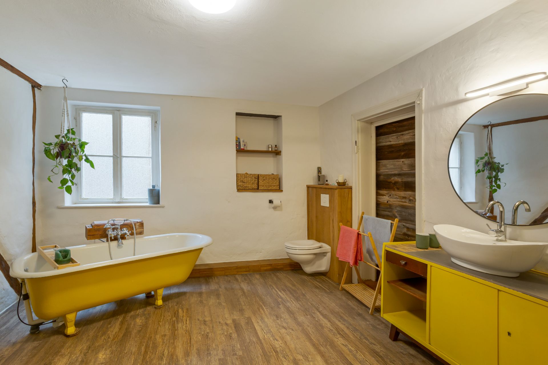 Helles Badezimmer mit gelber Badewanne, Holzfußboden und Spiegel über gelbem Waschbeckenunterschrank.