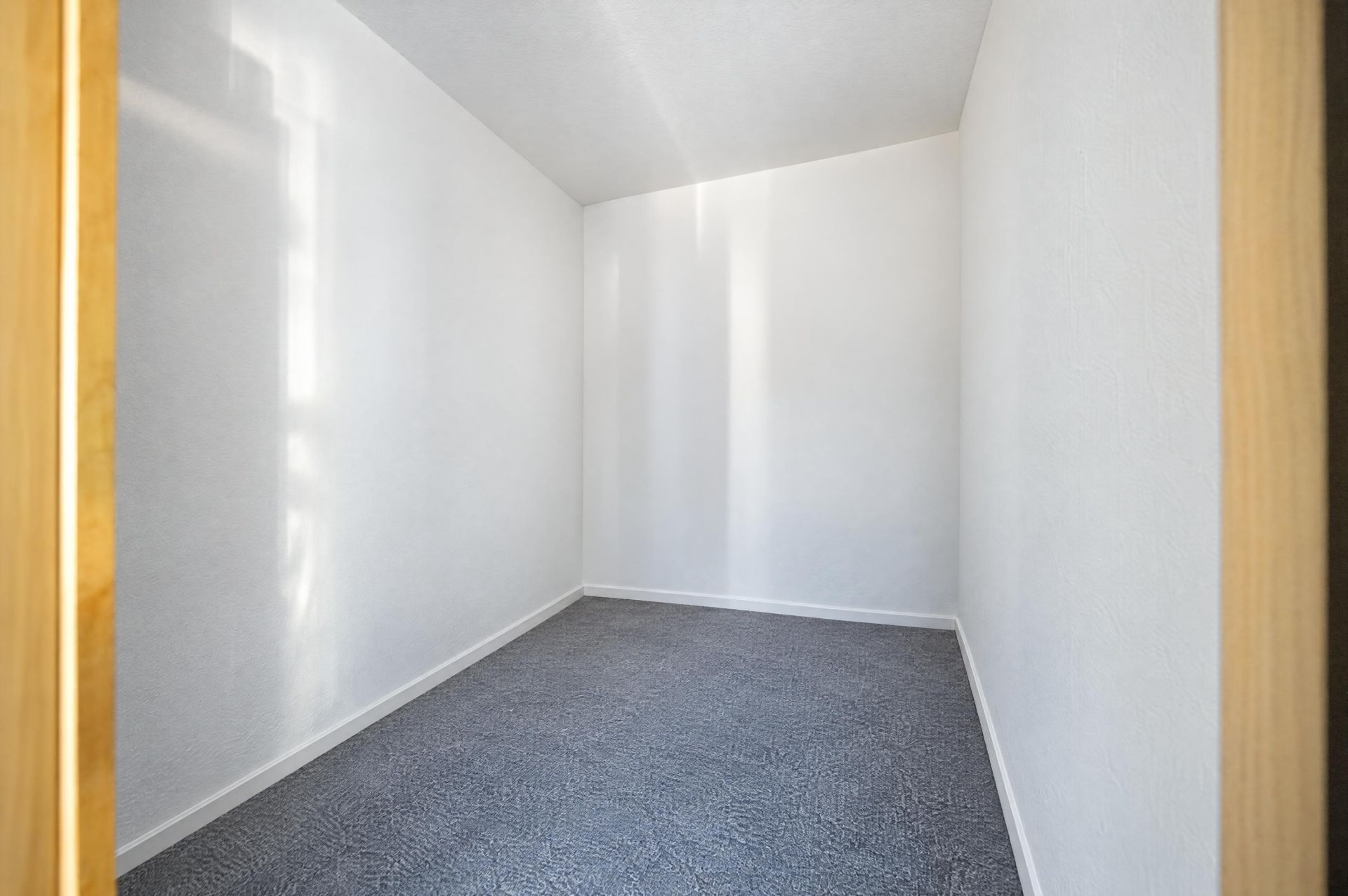 Leerer, kleiner Raum mit weißen Wänden und grauem Teppichboden.