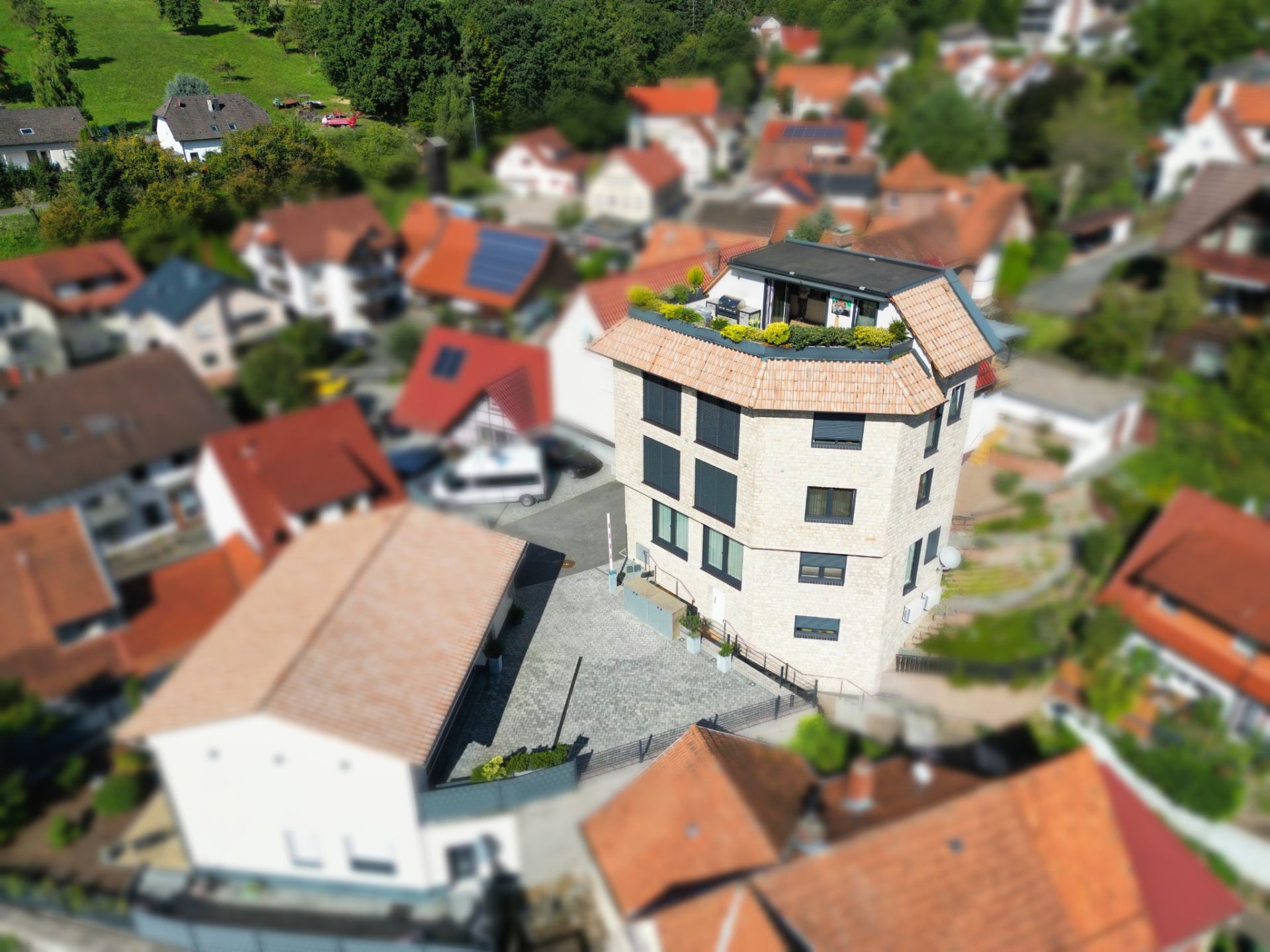 Mehrstöckiges Wohnhaus mit Flachdachterrasse inmitten anderer Häuser, von oben aufgenommen.