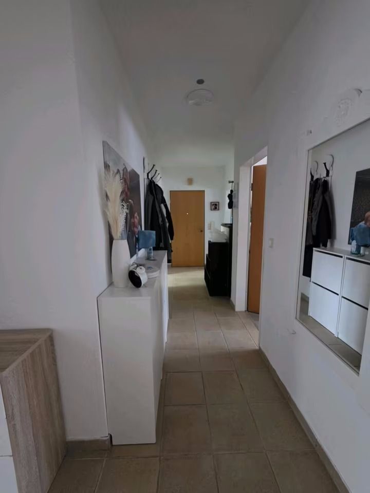 Heller Flur mit Garderobe, Spiegel, Kommode und Dekorationen an den weißen Wänden.