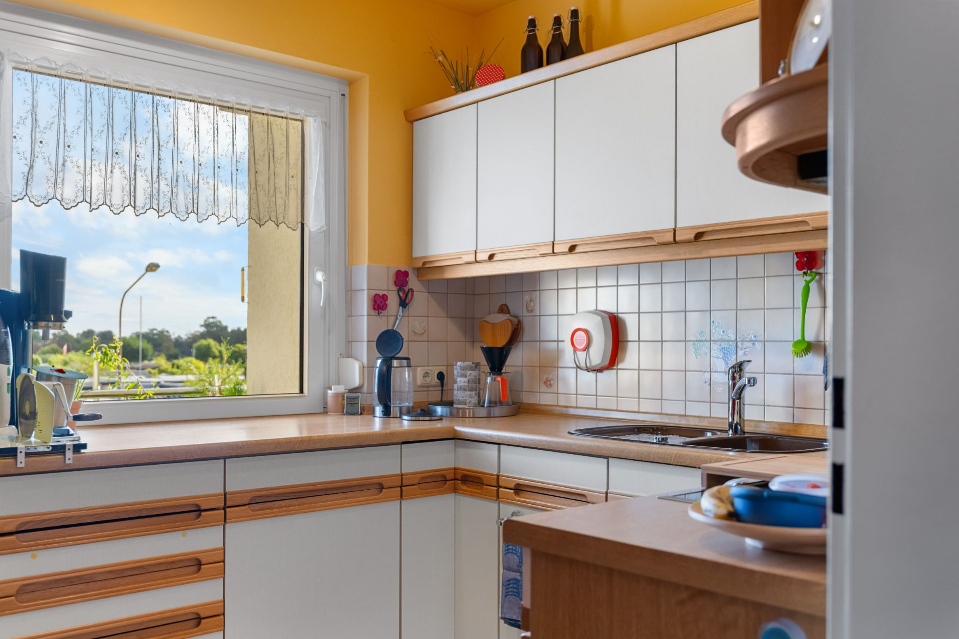 Helle Küche mit weißen Schränken, Holzarbeitsplatten und großem Fenster.