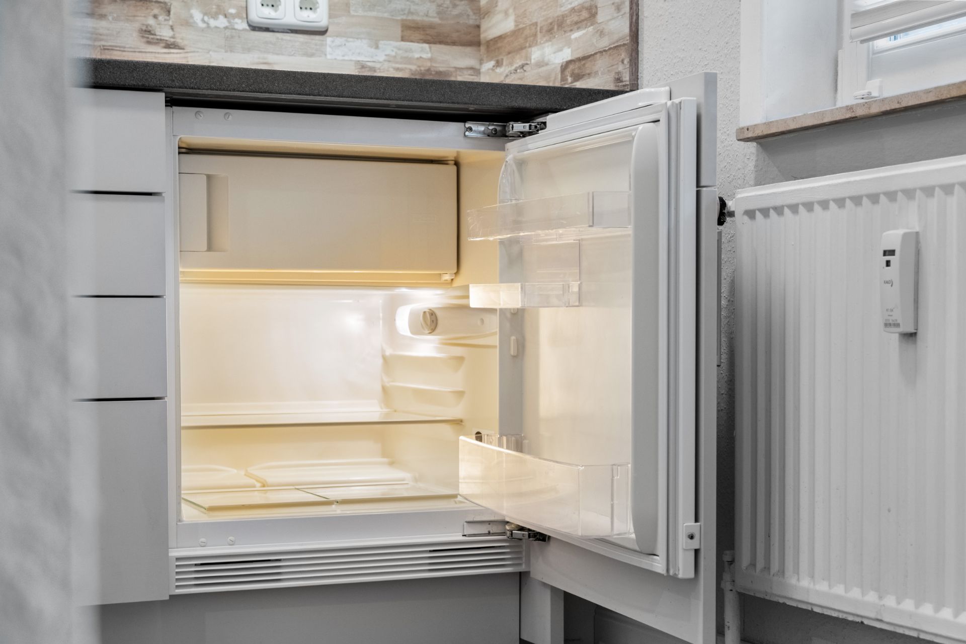 Ein leerer, geöffneter Kühlschrank in einer Küche, beleuchtet von innen.