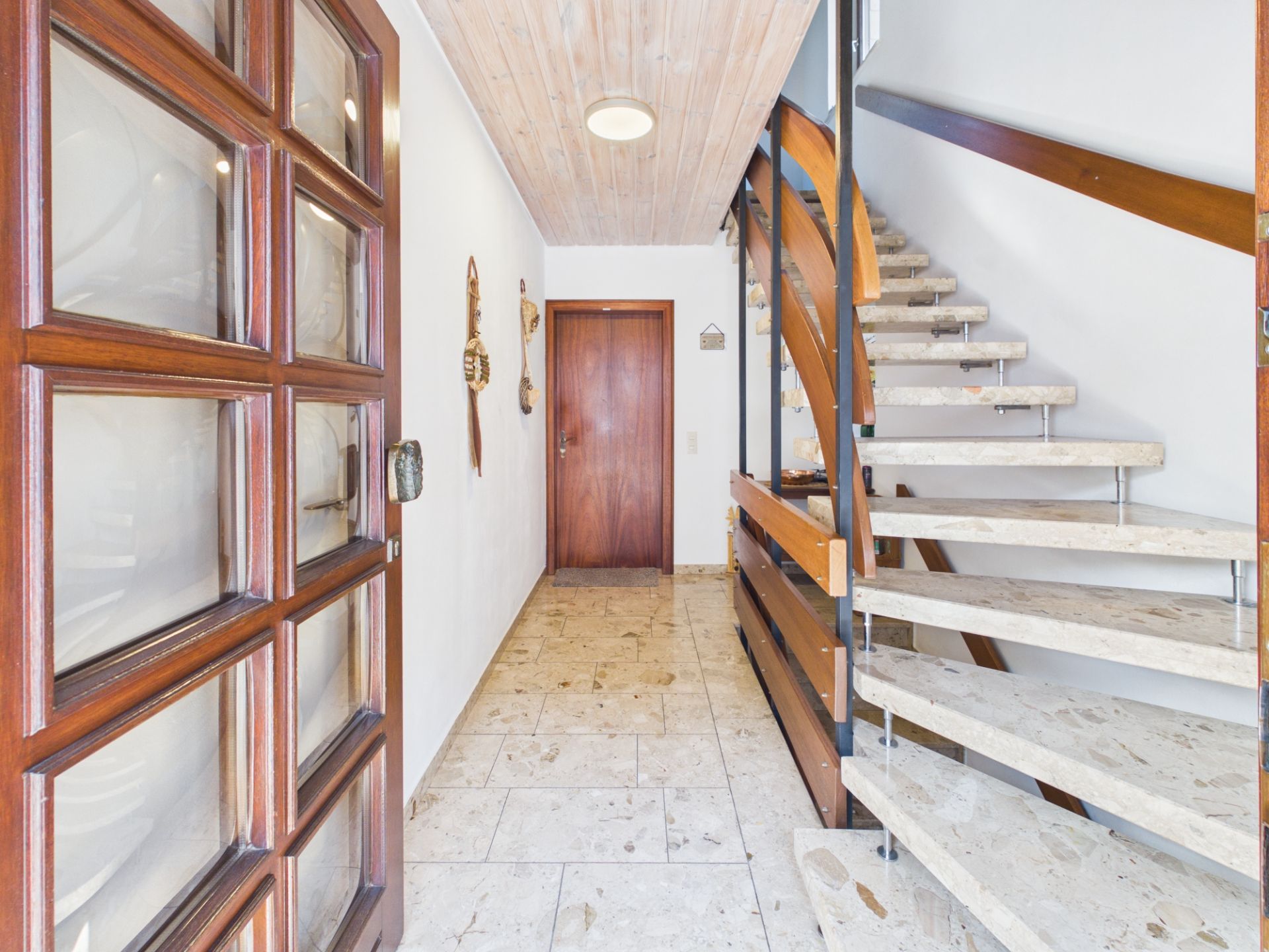 Heller Flur mit Marmortreppe und Holztür, Wanddekorationen und Fliesenboden.