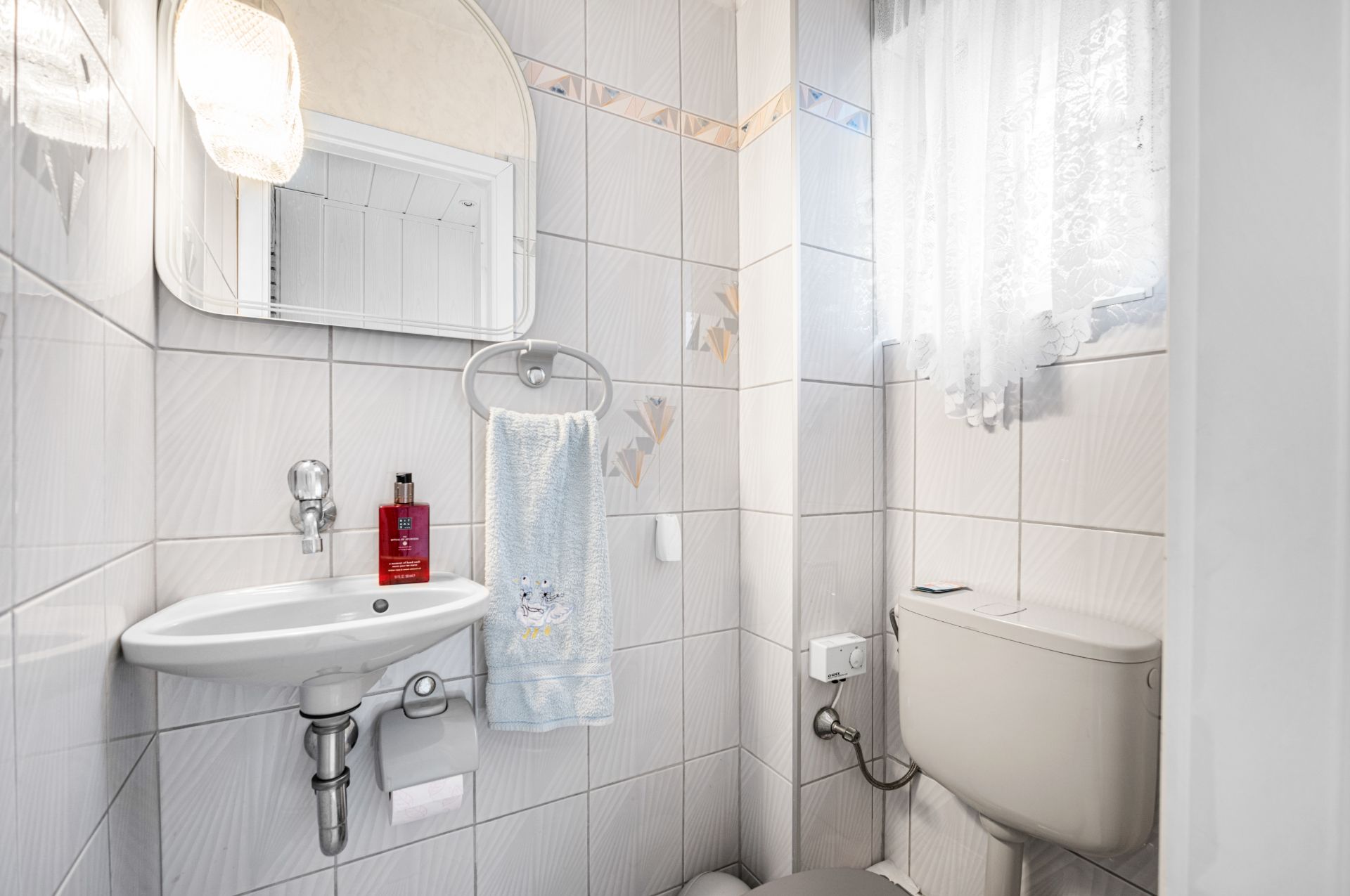 Kleines Badezimmer mit Waschbecken, Spiegel, Handtuch, Toilettenpapier und Toilette am Fenster.