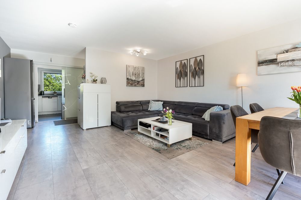 Helles Wohnzimmer mit grauem Ecksofa, Couchtisch und Esstisch mit Stühlen.