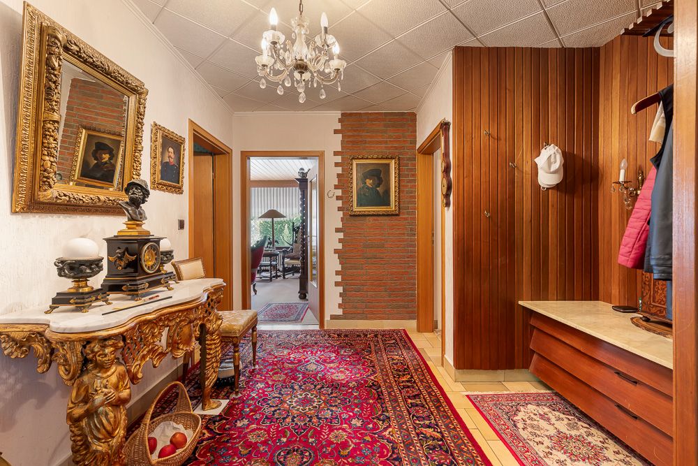Flur einer Wohnung mit Teppich, Kronleuchter, Spiegel und Holzgarderobe.