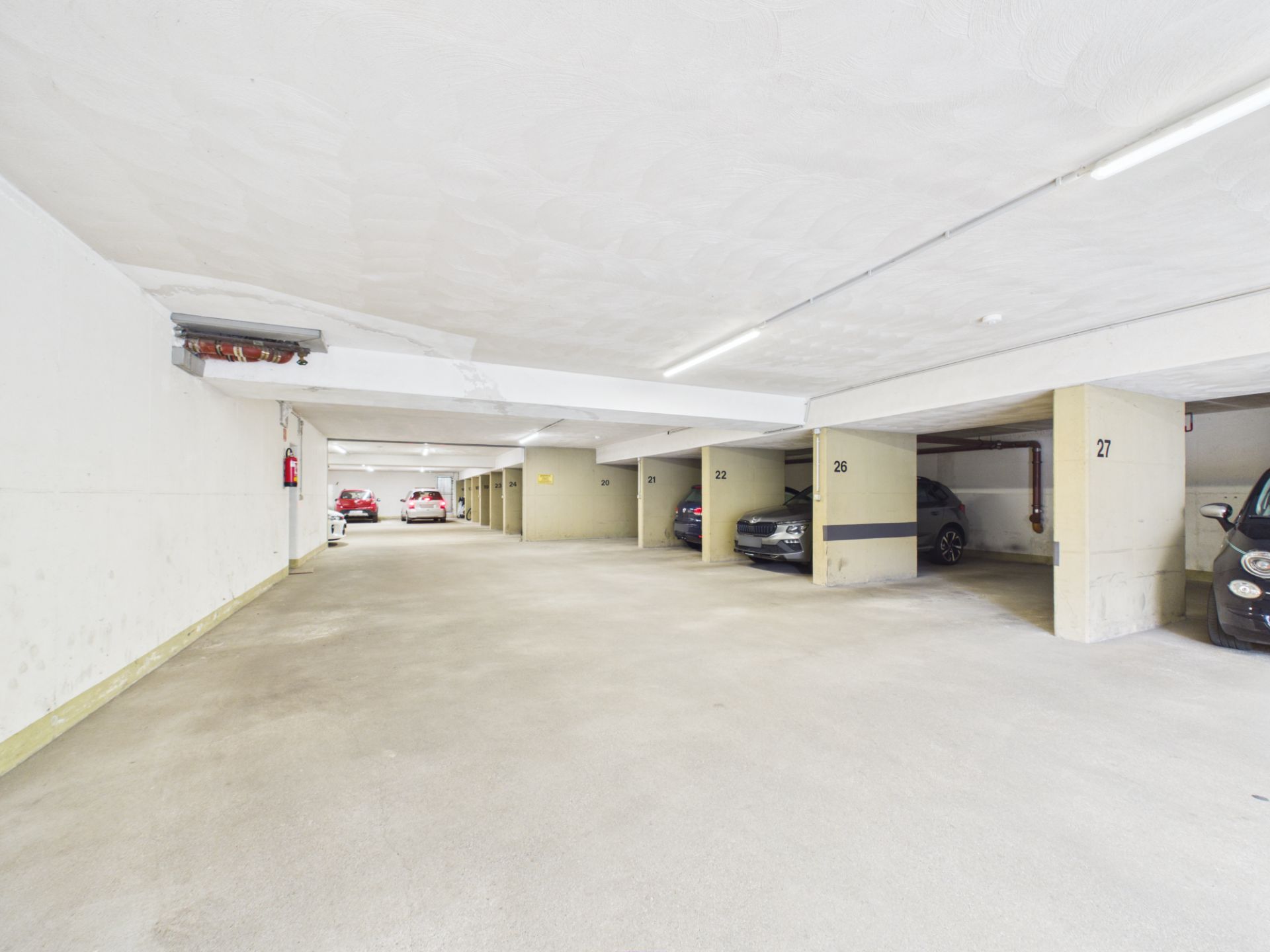 Helle Tiefgarage mit mehreren geparkten Autos und nummerierten Stellplätzen.