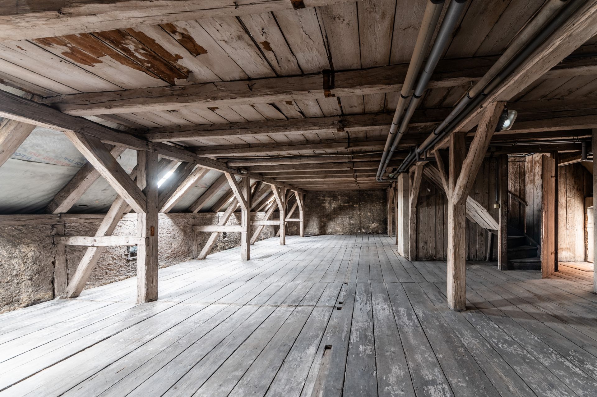 Alter, leerer Dachboden mit Holzbalken und Holzboden, sichtbarem Gebälk und Fenstern.