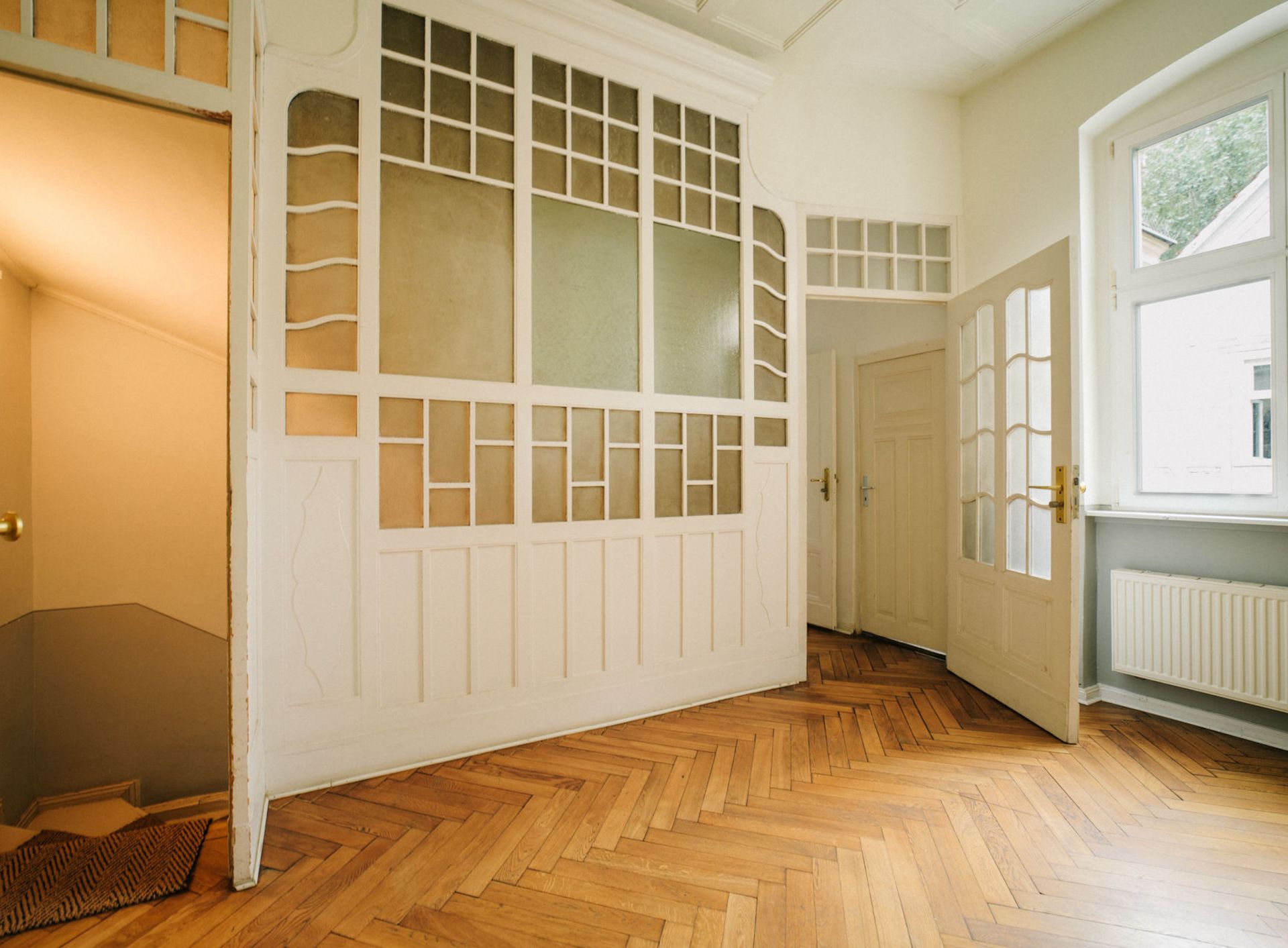 Heller Raum mit Holzboden, Glastüren, verglaster Trennwand und Treppe.