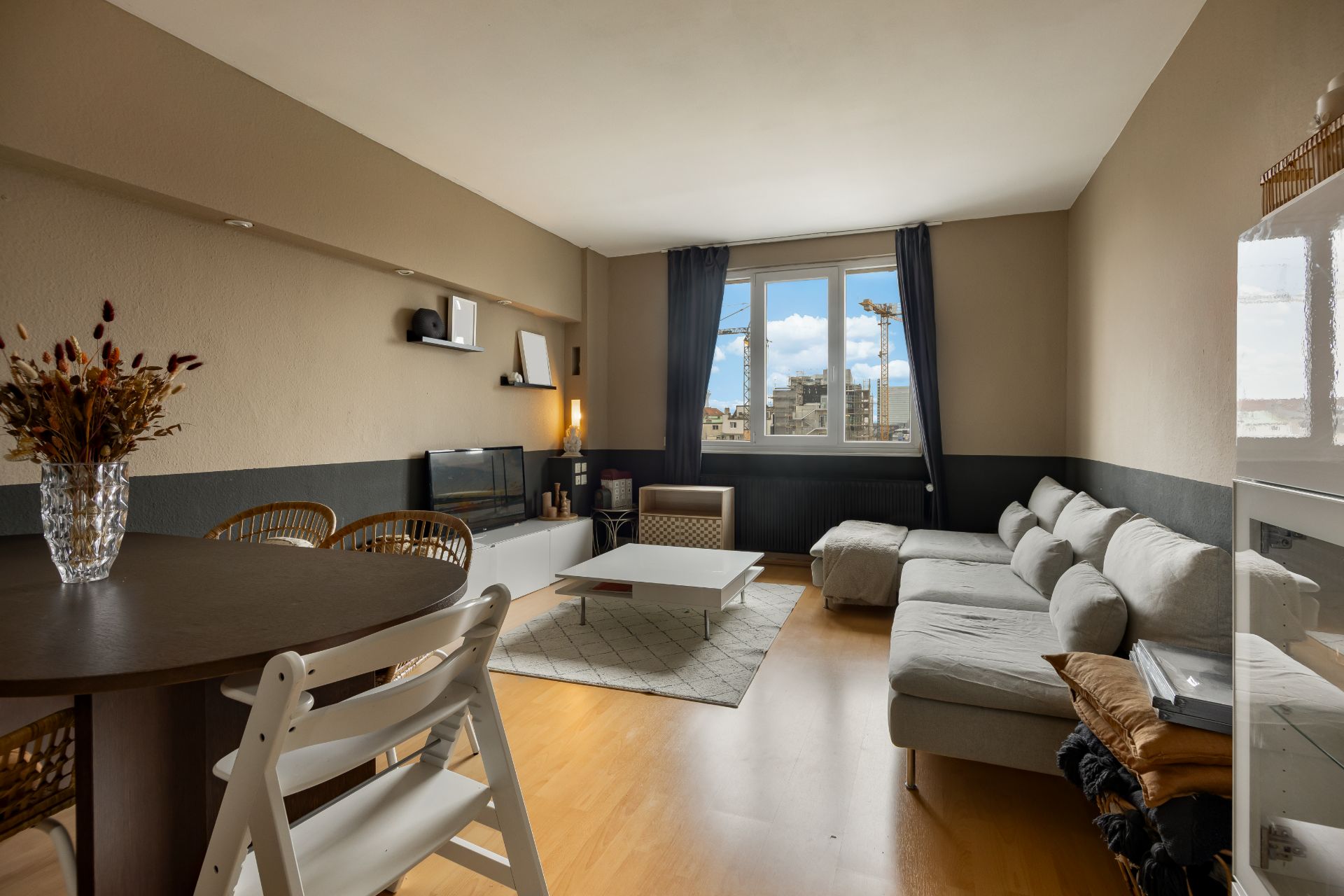 Helles Wohnzimmer mit Ecksofa, Couchtisch, Esstisch und großen Fenstern.