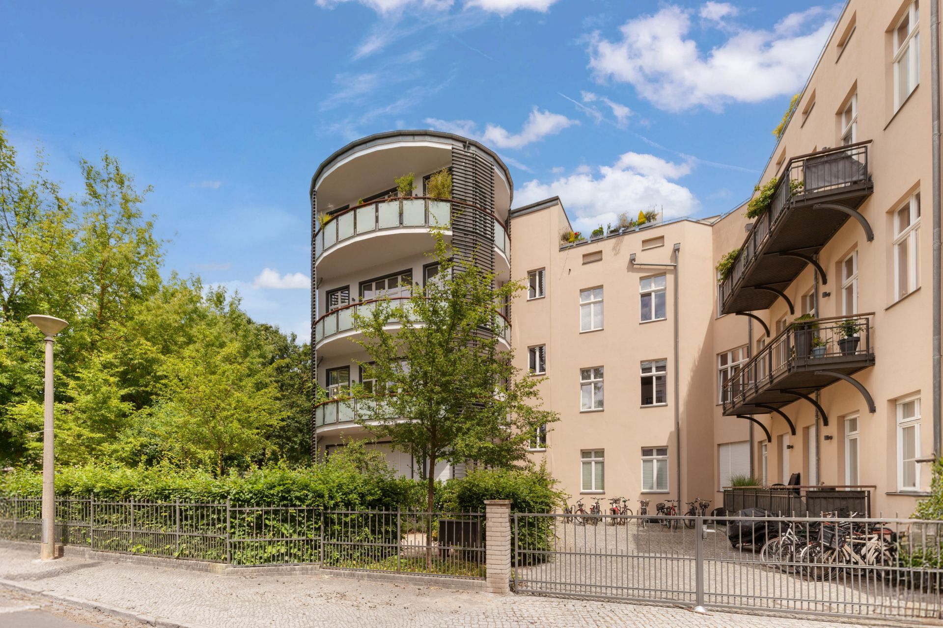 Mehrstöckiges Wohnhaus mit großen Balkonen, umgeben von Bäumen und Zaun.