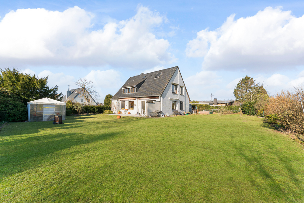 Einfamilienhaus mit großem Garten, Rasenfläche und Gewächshaus bei Tageslicht.