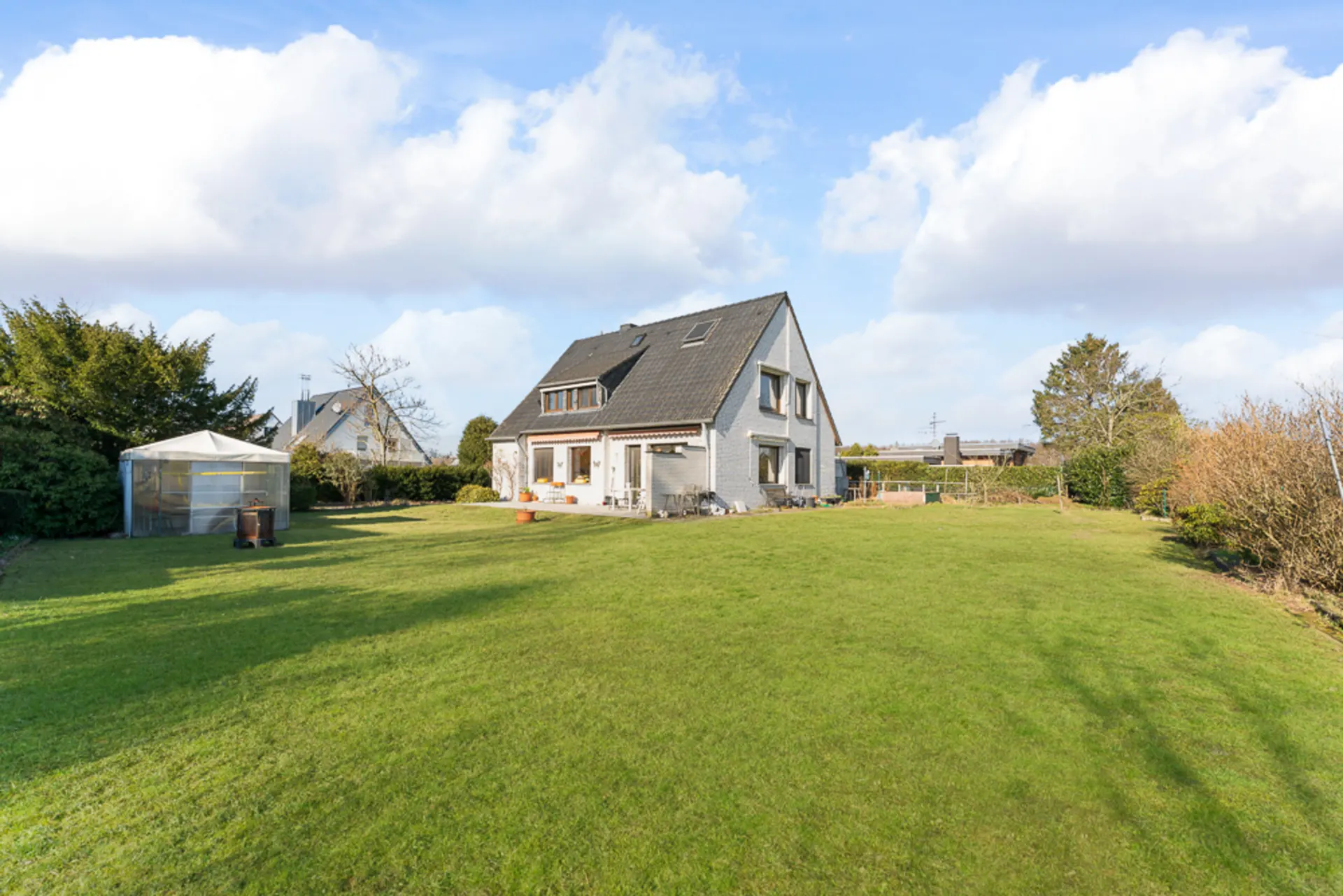 Einfamilienhaus mit großem Garten, Rasenfläche und Gewächshaus bei Tageslicht.