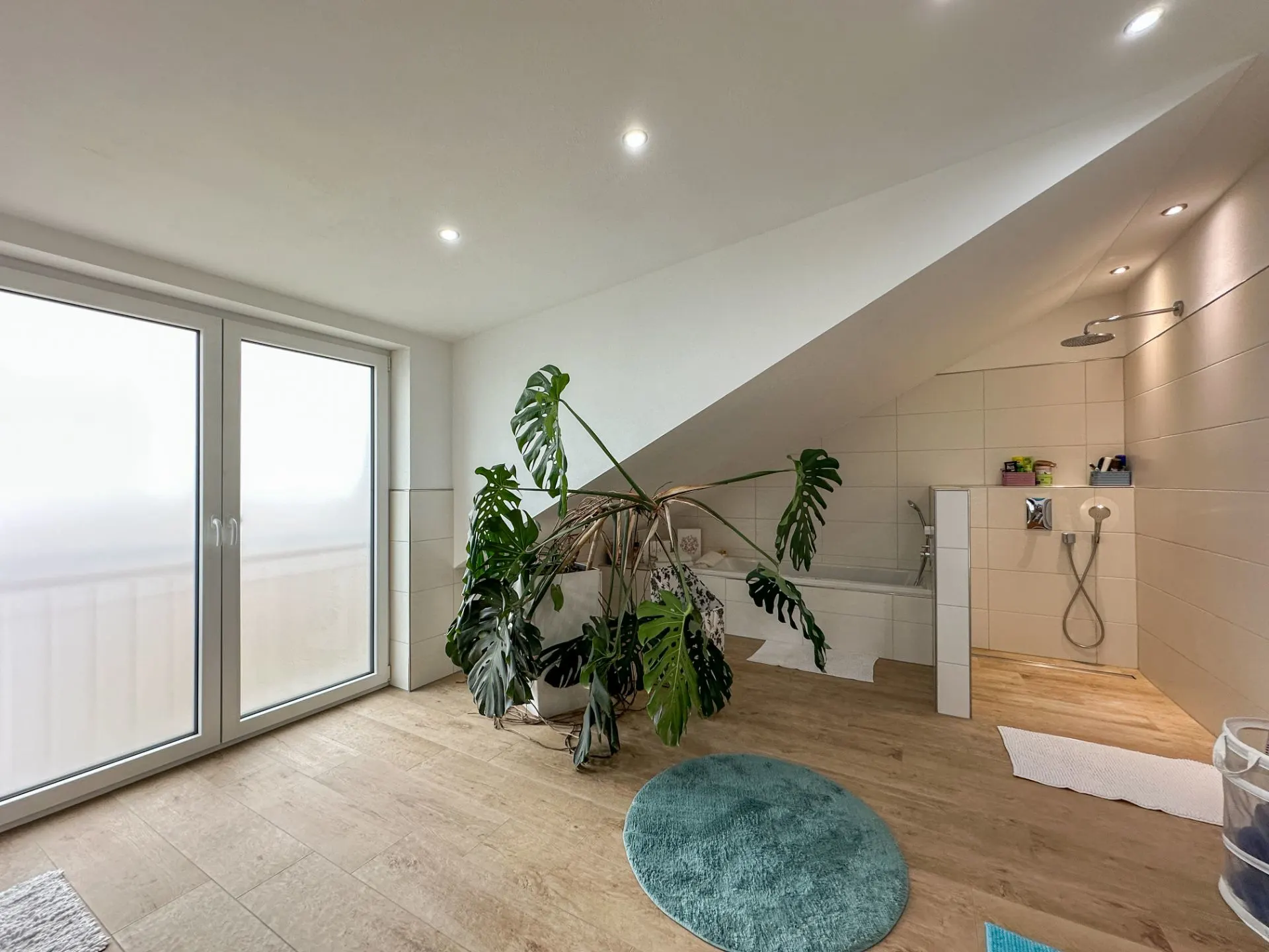 Modernes Badezimmer mit Dachschräge, großer Pflanze, Badewanne und Dusche, Fenster mit Milchglas.