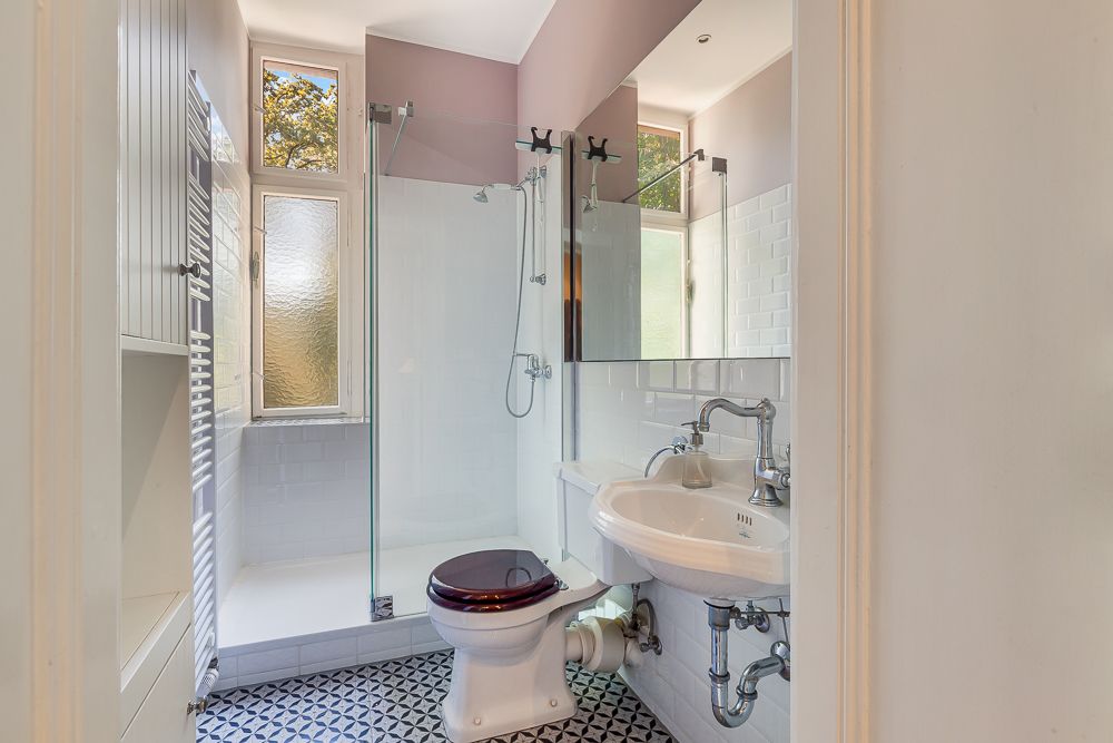 Helles Badezimmer mit Dusche, WC, Waschbecken und gemustertem Fliesenboden.