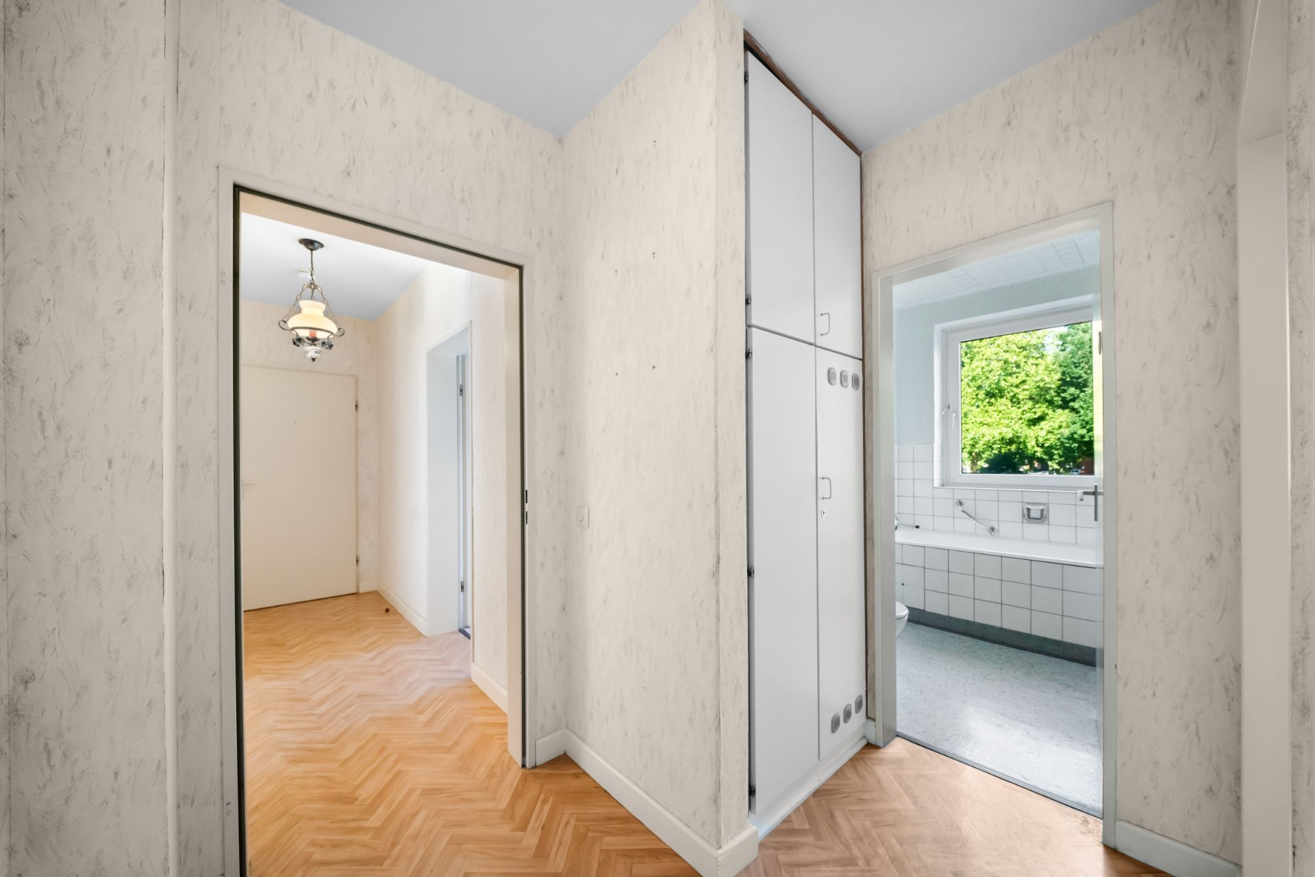 Flur mit Einbauschrank, Blick in ein Badezimmer und ein weiteres Zimmer mit Holzfußboden.